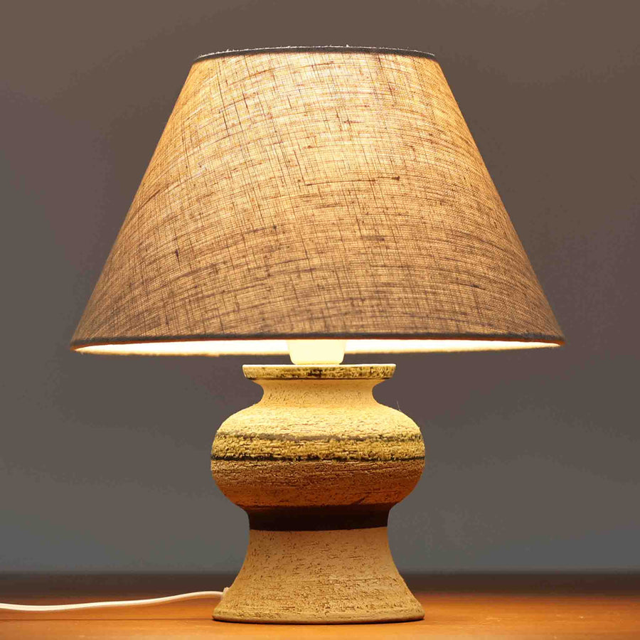 Axella製のこちらのテーブルランプは、素朴な陶土の質感と水平に重ねられた釉薬のグラデーションが生む落ち着いた佇まいが魅力で、ふくらみのある曲線的なベースと小ぶりなサイズ感が空間にさりげない温かみを添える北欧ビンテージ品です。リネンシェード越しに漏れる柔らかな灯りが陶肌の陰影をやさしく引き立て、デスクやベッドサイドなどにも取り入れやすく、経年で深まった素材の風合いが一点物ならではの味わいを感じさせてくれます。
