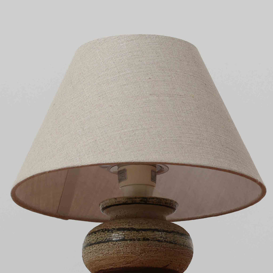 Axella製のこちらのテーブルランプは、素朴な陶土の質感と水平に重ねられた釉薬のグラデーションが生む落ち着いた佇まいが魅力で、ふくらみのある曲線的なベースと小ぶりなサイズ感が空間にさりげない温かみを添える北欧ビンテージ品です。リネンシェード越しに漏れる柔らかな灯りが陶肌の陰影をやさしく引き立て、デスクやベッドサイドなどにも取り入れやすく、経年で深まった素材の風合いが一点物ならではの味わいを感じさせてくれます。