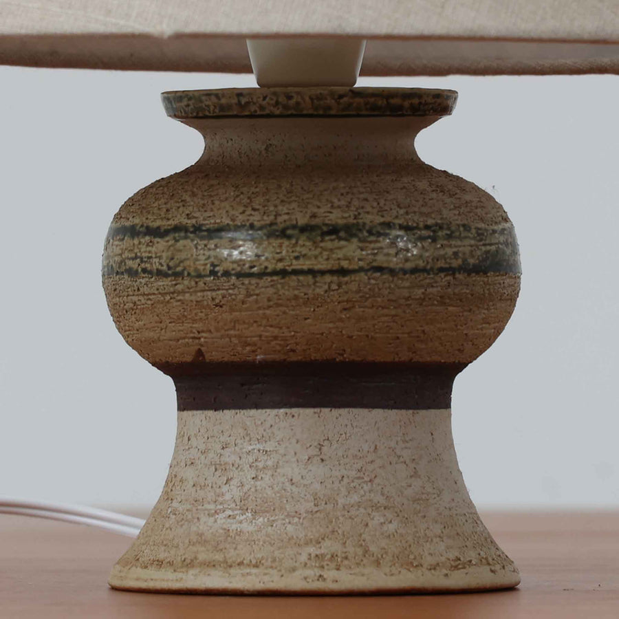 Axella製のこちらのテーブルランプは、素朴な陶土の質感と水平に重ねられた釉薬のグラデーションが生む落ち着いた佇まいが魅力で、ふくらみのある曲線的なベースと小ぶりなサイズ感が空間にさりげない温かみを添える北欧ビンテージ品です。リネンシェード越しに漏れる柔らかな灯りが陶肌の陰影をやさしく引き立て、デスクやベッドサイドなどにも取り入れやすく、経年で深まった素材の風合いが一点物ならではの味わいを感じさせてくれます。