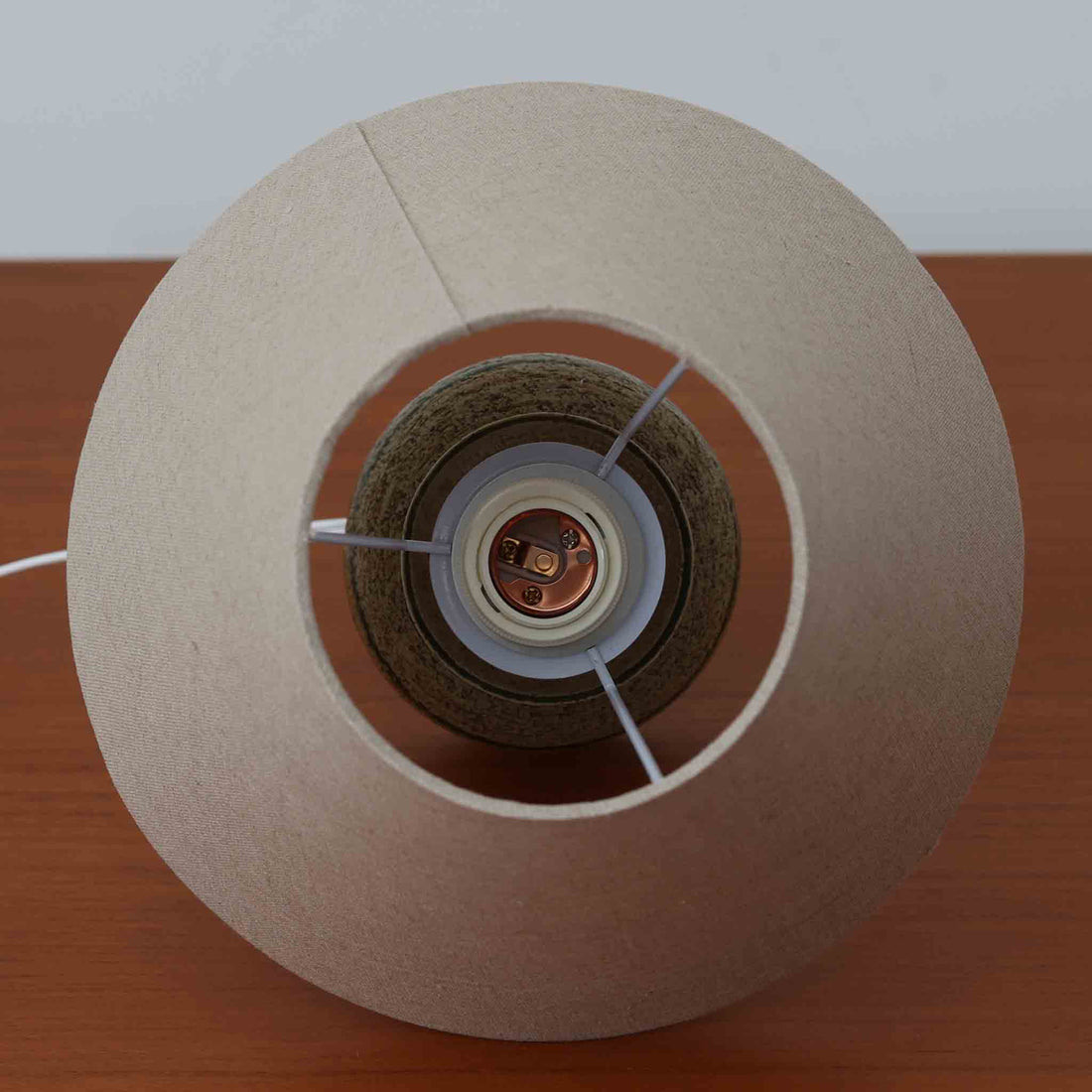 Axella製のこちらのテーブルランプは、素朴な陶土の質感と水平に重ねられた釉薬のグラデーションが生む落ち着いた佇まいが魅力で、ふくらみのある曲線的なベースと小ぶりなサイズ感が空間にさりげない温かみを添える北欧ビンテージ品です。リネンシェード越しに漏れる柔らかな灯りが陶肌の陰影をやさしく引き立て、デスクやベッドサイドなどにも取り入れやすく、経年で深まった素材の風合いが一点物ならではの味わいを感じさせてくれます。