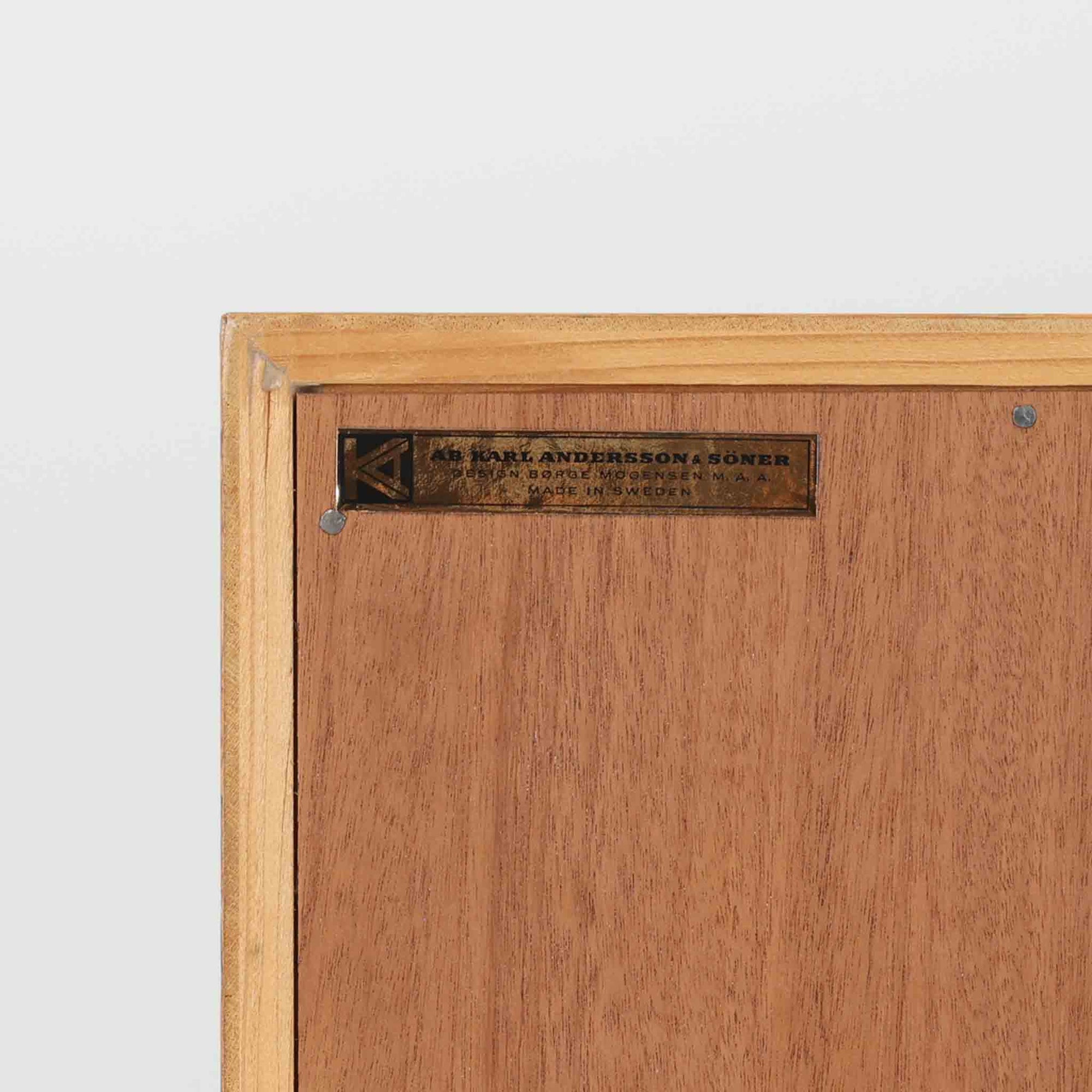 Borge Mogensenがデザインし、Karl Andersson &amp; Sonerが製作したブックシェルフです。オーク材の穏やかな木目を活かした直線的なフォルムは、無駄を削ぎ落としたモーエンセンらしい実直な美しさを感じさせます。幅135cmのゆとりあるサイズで、左右に分かれた収納部には可動棚を備え、書籍や器、オブジェまで柔軟にレイアウト可能。経年により深みを増した木肌が空間に温かみを添える、北欧ビンテージならではの堅実な一台です。