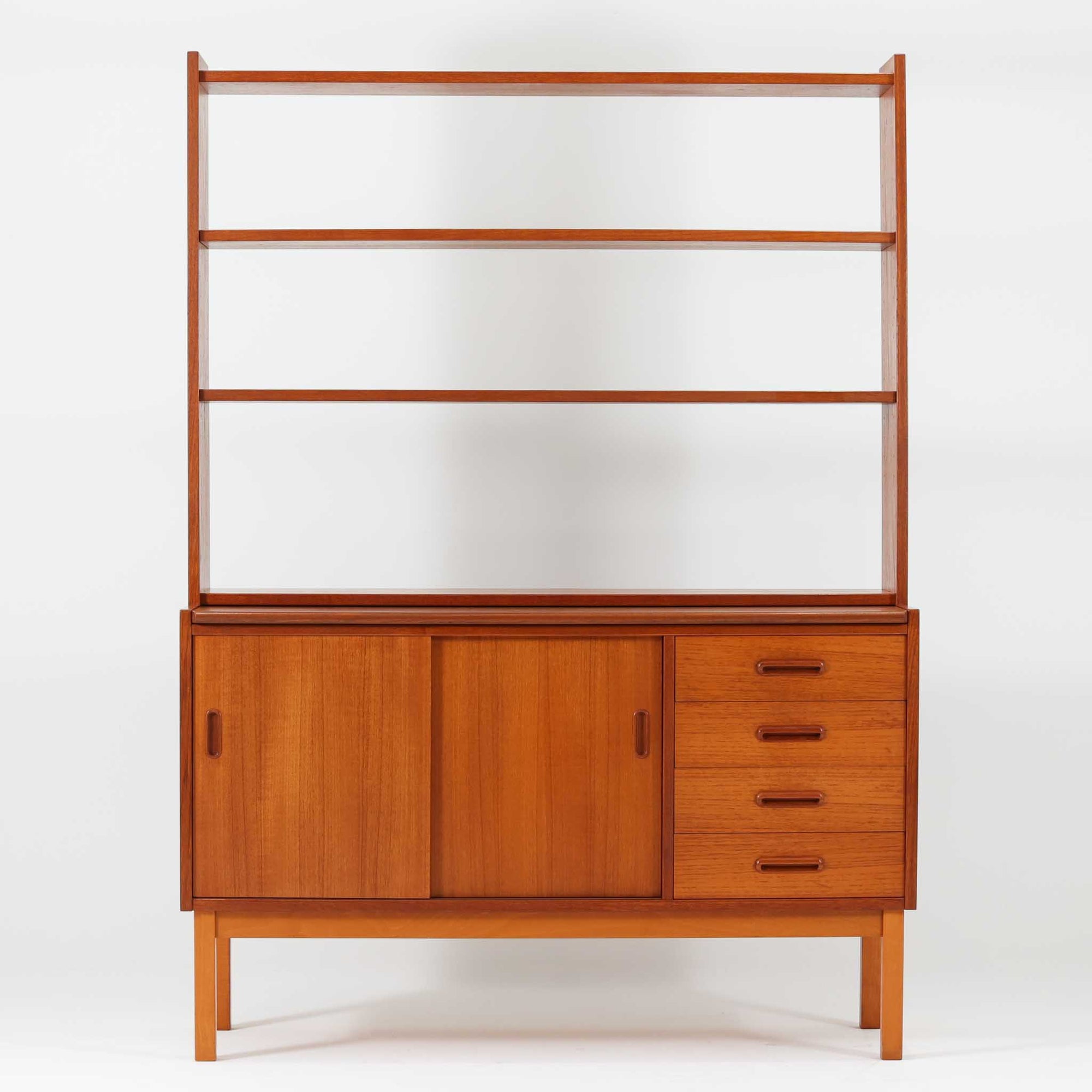 チーク材とビーチ材を組み合わせた北欧ビンテージらしい佇まいが魅力のディスプレイシェルフで、直線的で端正なフレーム構成と、木目の表情を活かした温かみのある質感が空間に落ち着きをもたらします。上部のオープン棚は器や書籍、オブジェの展示に適しており、下部には引き戸収納と引き出しを備えることで、見せる収納と隠す収納をバランス良く両立しています。脚付き構造により圧迫感が少なく、リビングやダイニング、書斎など幅広いシーンで活躍し、経年変化による色味の深まりも楽しめる一台です。