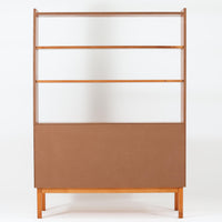 チーク材とビーチ材を組み合わせた北欧ビンテージらしい佇まいが魅力のディスプレイシェルフで、直線的で端正なフレーム構成と、木目の表情を活かした温かみのある質感が空間に落ち着きをもたらします。上部のオープン棚は器や書籍、オブジェの展示に適しており、下部には引き戸収納と引き出しを備えることで、見せる収納と隠す収納をバランス良く両立しています。脚付き構造により圧迫感が少なく、リビングやダイニング、書斎など幅広いシーンで活躍し、経年変化による色味の深まりも楽しめる一台です。