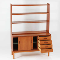 チーク材とビーチ材を組み合わせた北欧ビンテージらしい佇まいが魅力のディスプレイシェルフで、直線的で端正なフレーム構成と、木目の表情を活かした温かみのある質感が空間に落ち着きをもたらします。上部のオープン棚は器や書籍、オブジェの展示に適しており、下部には引き戸収納と引き出しを備えることで、見せる収納と隠す収納をバランス良く両立しています。脚付き構造により圧迫感が少なく、リビングやダイニング、書斎など幅広いシーンで活躍し、経年変化による色味の深まりも楽しめる一台です。