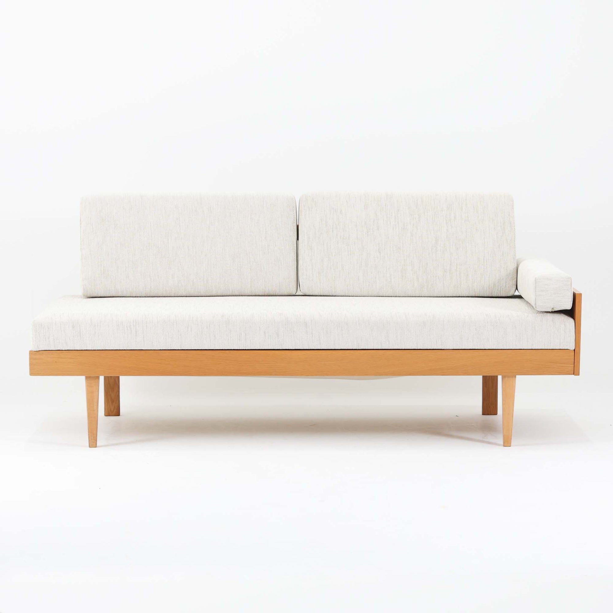 Ingmar Rellingがデザインし、EKORNESより発表されたSvane（スワン）デイベッドです。オーク材の明るく滑らかなフレームに、直線的な背もたれとすっきりとした脚部を組み合わせた端正な構造が特徴です。背もたれを上げると内部には帆布張りの収納部が備えられており、さらに背もたれを起こしてアーム部を伸ばすことでサイドテーブルとしても使用可能です。サイドテーブル部分に背クッションを載せることでベッドとしてもお使いいただけます。リビングやゲストルームなど多様な空間に適しており、張り替え済みのファブリックは上質な質感で空間にやわらかな印象を添えます。機能美と快適性を兼ね備えた、北欧ビンテージならではの名作です。