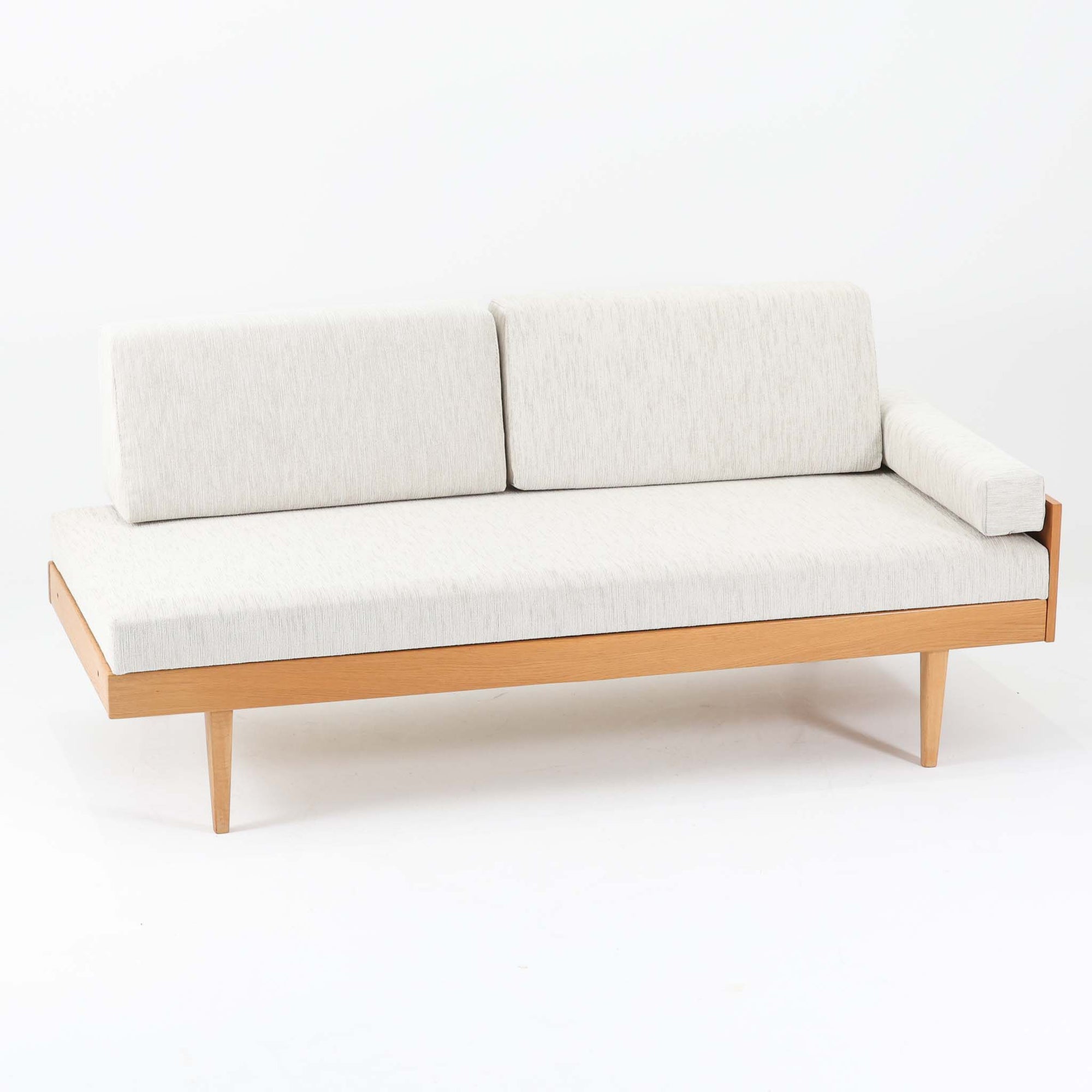 Ingmar Rellingがデザインし、EKORNESより発表されたSvane（スワン）デイベッドです。オーク材の明るく滑らかなフレームに、直線的な背もたれとすっきりとした脚部を組み合わせた端正な構造が特徴です。背もたれを上げると内部には帆布張りの収納部が備えられており、さらに背もたれを起こしてアーム部を伸ばすことでサイドテーブルとしても使用可能です。サイドテーブル部分に背クッションを載せることでベッドとしてもお使いいただけます。リビングやゲストルームなど多様な空間に適しており、張り替え済みのファブリックは上質な質感で空間にやわらかな印象を添えます。機能美と快適性を兼ね備えた、北欧ビンテージならではの名作です。
