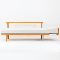 Ingmar Rellingがデザインし、EKORNESより発表されたSvane（スワン）デイベッドです。オーク材の明るく滑らかなフレームに、直線的な背もたれとすっきりとした脚部を組み合わせた端正な構造が特徴です。背もたれを上げると内部には帆布張りの収納部が備えられており、さらに背もたれを起こしてアーム部を伸ばすことでサイドテーブルとしても使用可能です。サイドテーブル部分に背クッションを載せることでベッドとしてもお使いいただけます。リビングやゲストルームなど多様な空間に適しており、張り替え済みのファブリックは上質な質感で空間にやわらかな印象を添えます。機能美と快適性を兼ね備えた、北欧ビンテージならではの名作です。