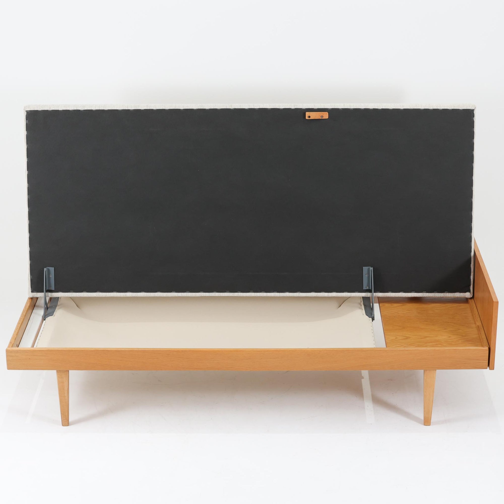 Ingmar Rellingがデザインし、EKORNESより発表されたSvane（スワン）デイベッドです。オーク材の明るく滑らかなフレームに、直線的な背もたれとすっきりとした脚部を組み合わせた端正な構造が特徴です。背もたれを上げると内部には帆布張りの収納部が備えられており、さらに背もたれを起こしてアーム部を伸ばすことでサイドテーブルとしても使用可能です。サイドテーブル部分に背クッションを載せることでベッドとしてもお使いいただけます。リビングやゲストルームなど多様な空間に適しており、張り替え済みのファブリックは上質な質感で空間にやわらかな印象を添えます。機能美と快適性を兼ね備えた、北欧ビンテージならではの名作です。