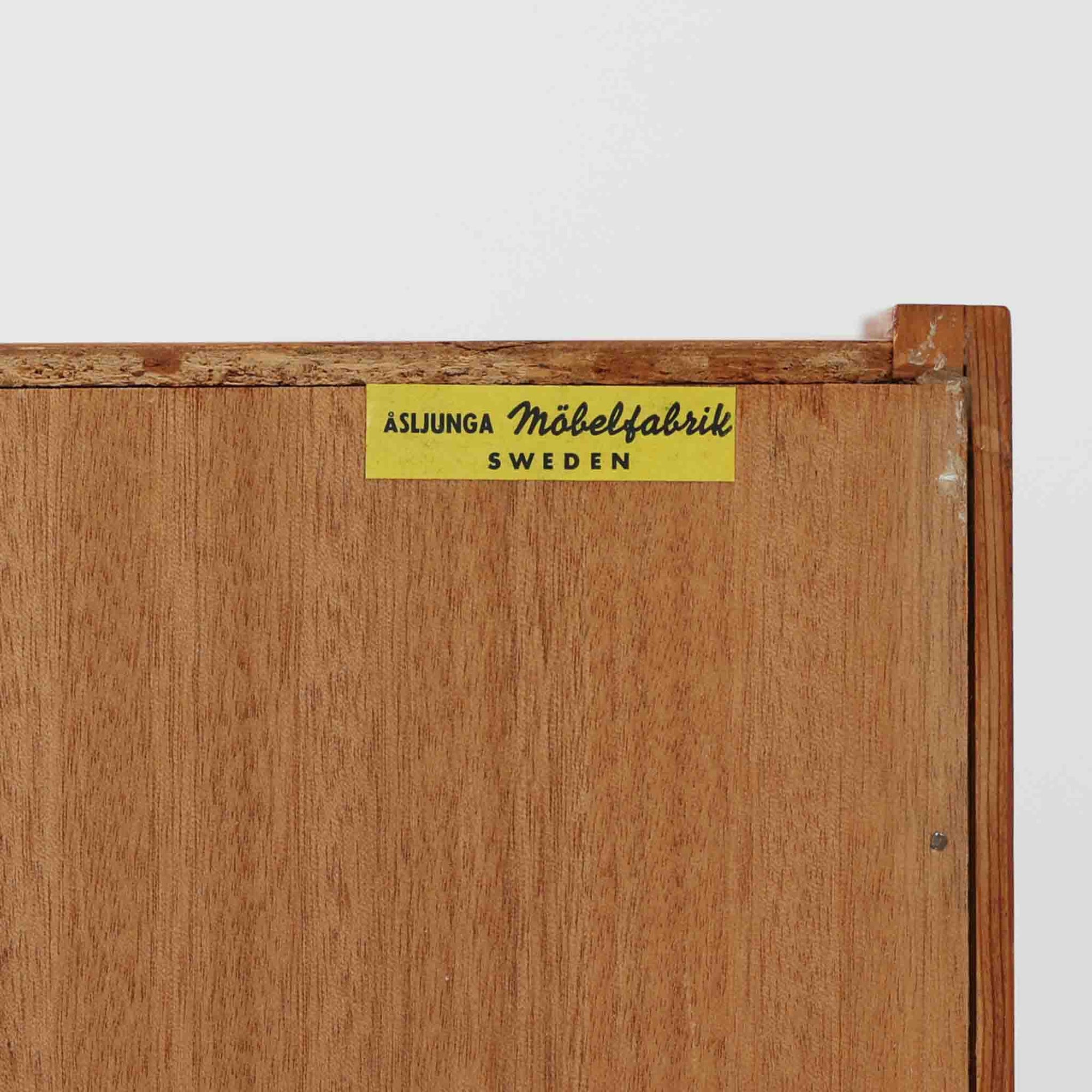 Asljunga Mobelfabrikによるディスプレイシェルフは、チーク材とビーチ材を組み合わせた端正な佇まいが魅力の北欧ビンテージ家具です。上段はオープンシェルフ構造で、棚板を活かした見せる収納が楽しめ、下段には引き戸式の収納部を備えることで実用性も確保されています。直線的で無駄のないフォルムに、掘り込み式の取っ手や脚部の軽やかなバランスが北欧らしい品の良さを添え、幅79cmの程よいサイズ感はリビングやダイニング、書斎など幅広い空間に取り入れやすく、経年変化によって深みを増した木肌と丁寧な造りが静かな存在感を放つ一台です。