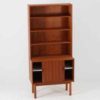 Asljunga Mobelfabrikによるディスプレイシェルフは、チーク材とビーチ材を組み合わせた端正な佇まいが魅力の北欧ビンテージ家具です。上段はオープンシェルフ構造で、棚板を活かした見せる収納が楽しめ、下段には引き戸式の収納部を備えることで実用性も確保されています。直線的で無駄のないフォルムに、掘り込み式の取っ手や脚部の軽やかなバランスが北欧らしい品の良さを添え、幅79cmの程よいサイズ感はリビングやダイニング、書斎など幅広い空間に取り入れやすく、経年変化によって深みを増した木肌と丁寧な造りが静かな存在感を放つ一台です。