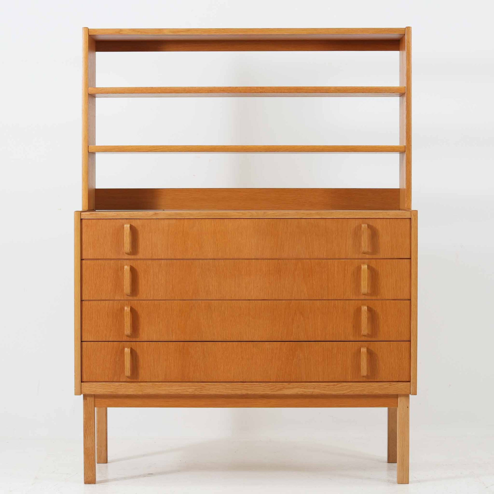 B. FridhagenがBodaforsのために手掛けたディスプレイシェルフは、端正なプロポーションと実用性を兼ね備えたスウェーデン製ビンテージ家具です。上部は抜け感のあるオープン棚構造で、器や書籍、オブジェなどを軽やかに飾ることができ、下部には4段の引き出しを備え、日常使いの収納にも対応します。オーク材ならではの明るく上品な木肌と、直線を基調とした構成が北欧らしい落ち着いた印象を生み、空間をすっきりとまとめてくれます。幅90cm、高さ122cmの小ぶりなサイズ感で、ダイニングやリビング、書斎など幅広いシーンに取り入れやすく、経年変化による木の表情も楽しめる一台です。