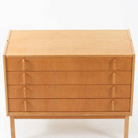 B. FridhagenがBodaforsのために手掛けたディスプレイシェルフは、端正なプロポーションと実用性を兼ね備えたスウェーデン製ビンテージ家具です。上部は抜け感のあるオープン棚構造で、器や書籍、オブジェなどを軽やかに飾ることができ、下部には4段の引き出しを備え、日常使いの収納にも対応します。オーク材ならではの明るく上品な木肌と、直線を基調とした構成が北欧らしい落ち着いた印象を生み、空間をすっきりとまとめてくれます。幅90cm、高さ122cmの小ぶりなサイズ感で、ダイニングやリビング、書斎など幅広いシーンに取り入れやすく、経年変化による木の表情も楽しめる一台です。