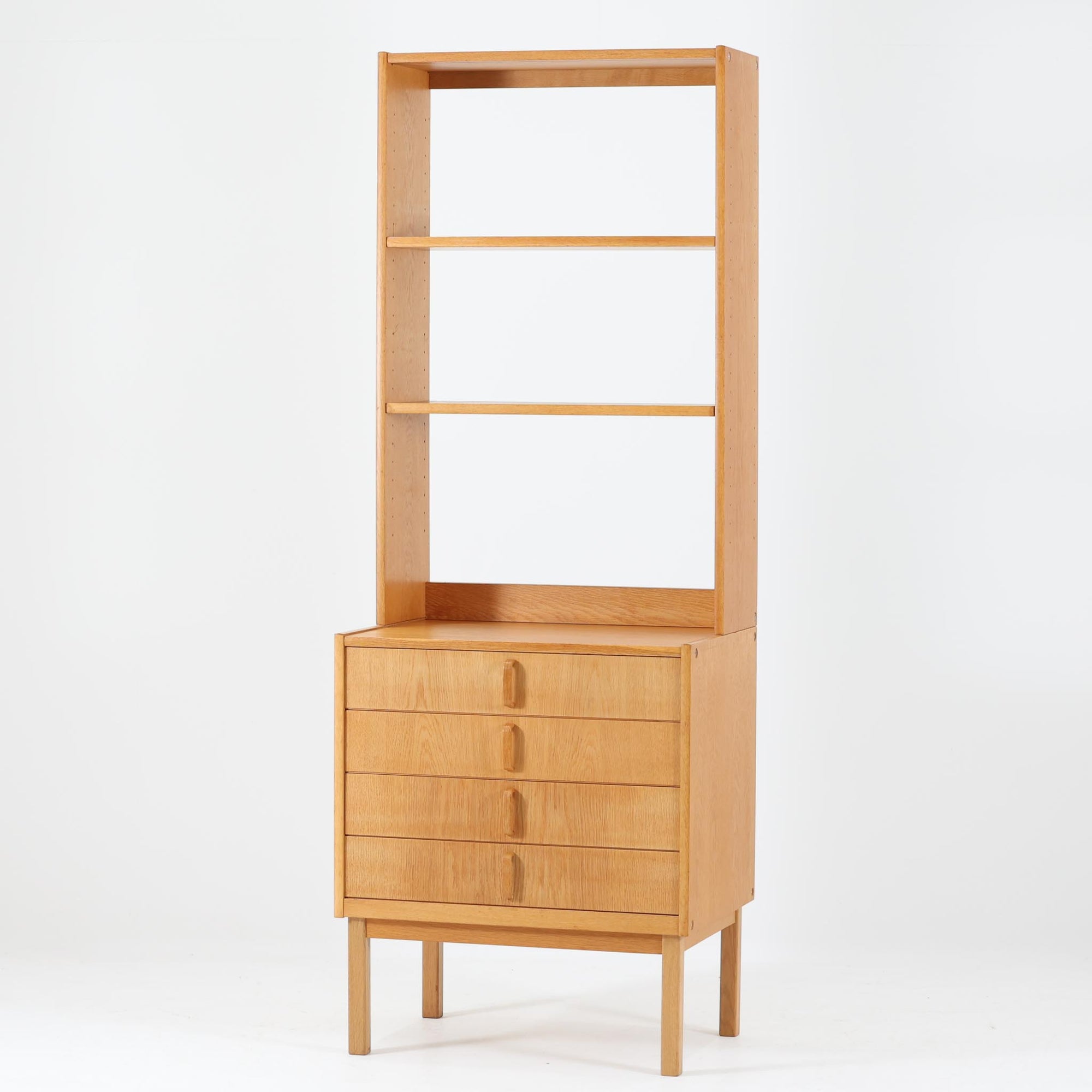 B. Fridhagenがデザインし、Bodafors社により1963年に製作されたスリムシェルフです。オーク材のやわらかな木目と明るい色合いが空間に温もりをもたらし、上部のオープン棚と下部の4段引き出しを備えた実用的な構成が魅力。幅63cmのすっきりとしたサイズで、書斎やリビングの一角にも取り入れやすい一台です。直線的で端正なフォルムと丁寧なつくりから、北欧ビンテージならではの機能美と経年の味わいを感じられる逸品です。