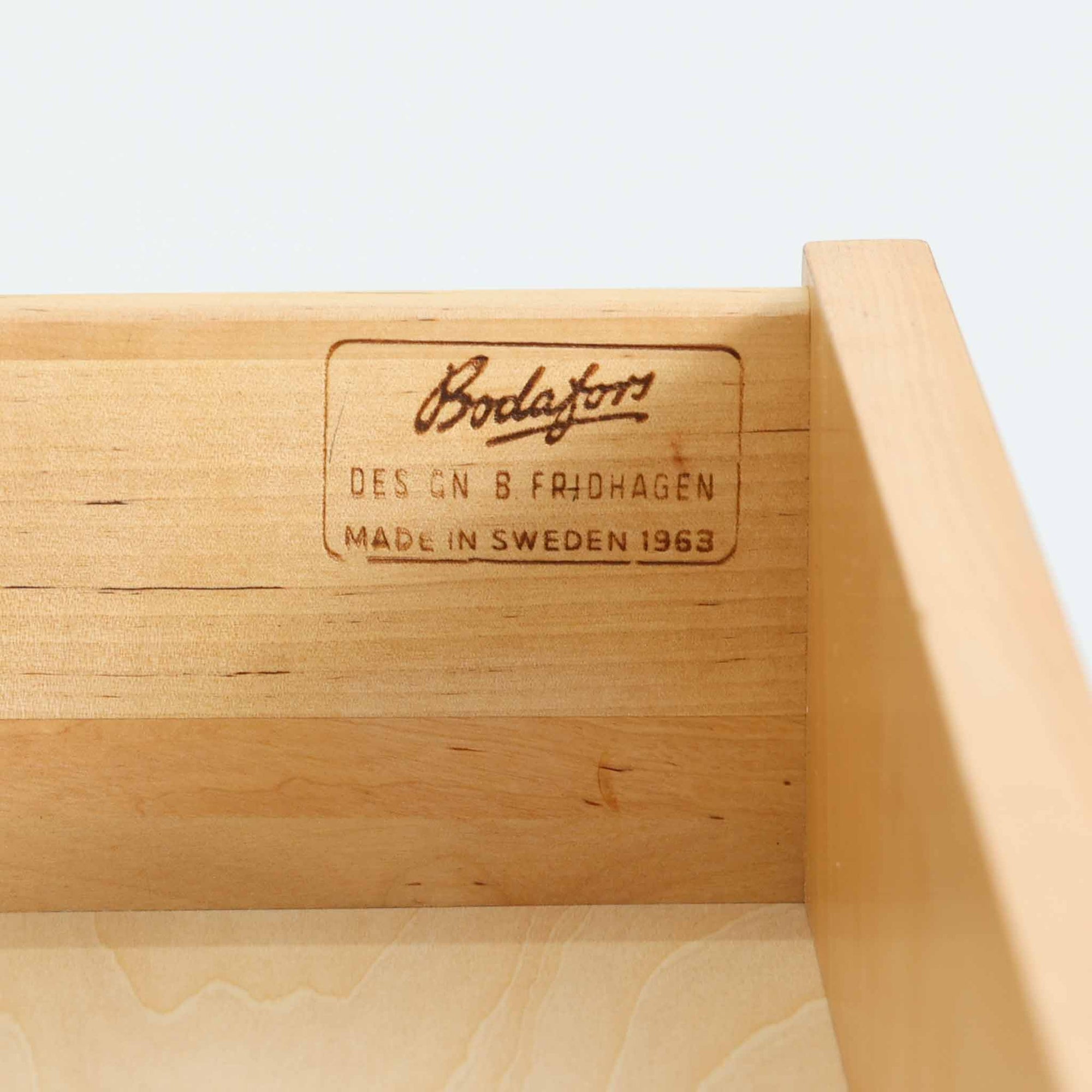 B. Fridhagenがデザインし、Bodafors社により1963年に製作されたスリムシェルフです。オーク材のやわらかな木目と明るい色合いが空間に温もりをもたらし、上部のオープン棚と下部の4段引き出しを備えた実用的な構成が魅力。幅63cmのすっきりとしたサイズで、書斎やリビングの一角にも取り入れやすい一台です。直線的で端正なフォルムと丁寧なつくりから、北欧ビンテージならではの機能美と経年の味わいを感じられる逸品です。