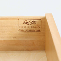 B. Fridhagenがデザインし、Bodafors社により1963年に製作されたスリムシェルフです。オーク材のやわらかな木目と明るい色合いが空間に温もりをもたらし、上部のオープン棚と下部の4段引き出しを備えた実用的な構成が魅力。幅63cmのすっきりとしたサイズで、書斎やリビングの一角にも取り入れやすい一台です。直線的で端正なフォルムと丁寧なつくりから、北欧ビンテージならではの機能美と経年の味わいを感じられる逸品です。