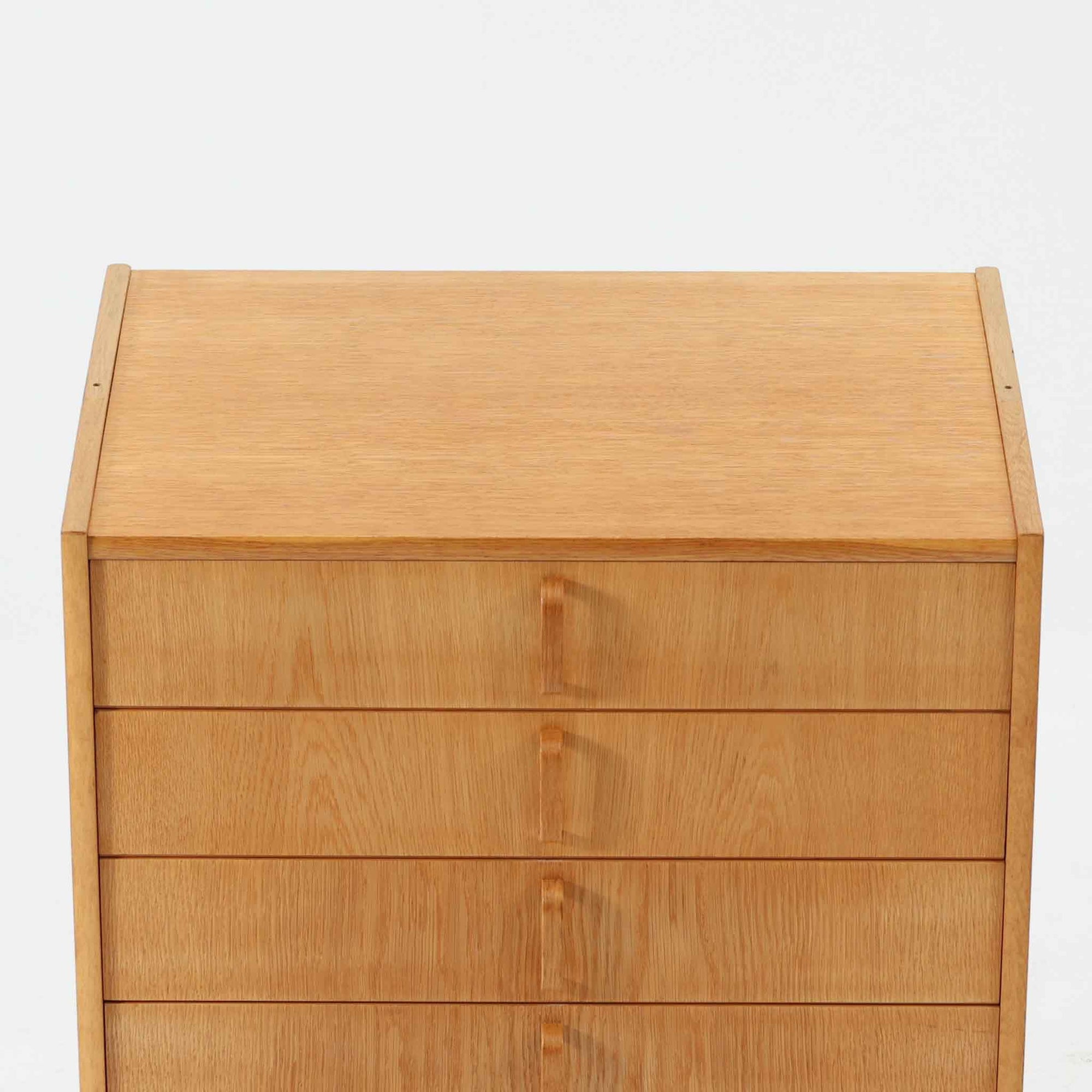 B. Fridhagenがデザインし、Bodafors社により1963年に製作されたスリムシェルフです。オーク材のやわらかな木目と明るい色合いが空間に温もりをもたらし、上部のオープン棚と下部の4段引き出しを備えた実用的な構成が魅力。幅63cmのすっきりとしたサイズで、書斎やリビングの一角にも取り入れやすい一台です。直線的で端正なフォルムと丁寧なつくりから、北欧ビンテージならではの機能美と経年の味わいを感じられる逸品です。