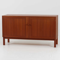 Nils JonssonがTroedsのためにデザインした「Domi Monte」モデルのキャビネットは、チーク材の豊かな木目と端正な框扉が魅力の北欧ビンテージ家具で、内部には可動棚を備えた左右対称の収納スペースが広がり食器や書類、小物類をすっきりと整理でき、チーク材をジョイントした鍵が細部の意匠性を高めつつ、直線的でシンプルな構造に細身の脚部を組み合わせることで軽やかな印象を生み出し、1960年代スウェーデン家具らしい上質で実用性の高いデザインが空間に落ち着いた存在感を添え、経年で深まった木肌の美しさも相まってリビングやダイニングのサイド収納として幅広く活躍する一台です。