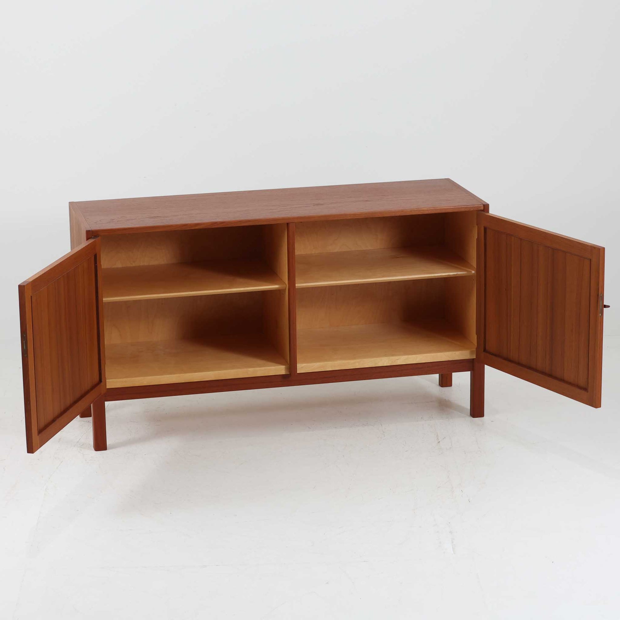 Nils JonssonがTroedsのためにデザインした「Domi Monte」モデルのキャビネットは、チーク材の豊かな木目と端正な框扉が魅力の北欧ビンテージ家具で、内部には可動棚を備えた左右対称の収納スペースが広がり食器や書類、小物類をすっきりと整理でき、チーク材をジョイントした鍵が細部の意匠性を高めつつ、直線的でシンプルな構造に細身の脚部を組み合わせることで軽やかな印象を生み出し、1960年代スウェーデン家具らしい上質で実用性の高いデザインが空間に落ち着いた存在感を添え、経年で深まった木肌の美しさも相まってリビングやダイニングのサイド収納として幅広く活躍する一台です。