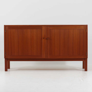 Nils JonssonがTroedsのためにデザインした「Domi Monte」モデルのキャビネットは、チーク材の豊かな木目と端正な框扉が魅力の北欧ビンテージ家具で、内部には可動棚を備えた左右対称の収納スペースが広がり食器や書類、小物類をすっきりと整理でき、チーク材をジョイントした鍵が細部の意匠性を高めつつ、直線的でシンプルな構造に細身の脚部を組み合わせることで軽やかな印象を生み出し、1960年代スウェーデン家具らしい上質で実用性の高いデザインが空間に落ち着いた存在感を添え、経年で深まった木肌の美しさも相まってリビングやダイニングのサイド収納として幅広く活躍する一台です。