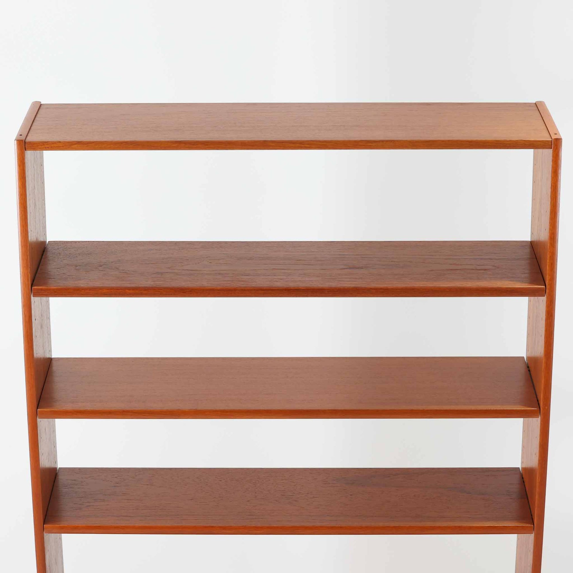 B.フリードホーゲンがデザインし、Bodafors社により製作された北欧ビンテージのディスプレイシェルフです。チーク材の美しい木目を活かした縦に伸びる端正なフレーム構成が印象的で、オープン棚と下部収納を組み合わせた実用性の高いデザインとなっています。上段は抜け感のある棚板構造で、書籍や器、オブジェを軽やかに飾ることができ、下段の引き戸収納は生活感の出やすい物をすっきりと収められます。脚付きによる軽快な佇まいと、経年変化によって深みを増した素材感が、空間に北欧ビンテージならではの落ち着いた存在感を与えます。