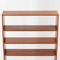 B.フリードホーゲンがデザインし、Bodafors社により製作された北欧ビンテージのディスプレイシェルフです。チーク材の美しい木目を活かした縦に伸びる端正なフレーム構成が印象的で、オープン棚と下部収納を組み合わせた実用性の高いデザインとなっています。上段は抜け感のある棚板構造で、書籍や器、オブジェを軽やかに飾ることができ、下段の引き戸収納は生活感の出やすい物をすっきりと収められます。脚付きによる軽快な佇まいと、経年変化によって深みを増した素材感が、空間に北欧ビンテージならではの落ち着いた存在感を与えます。