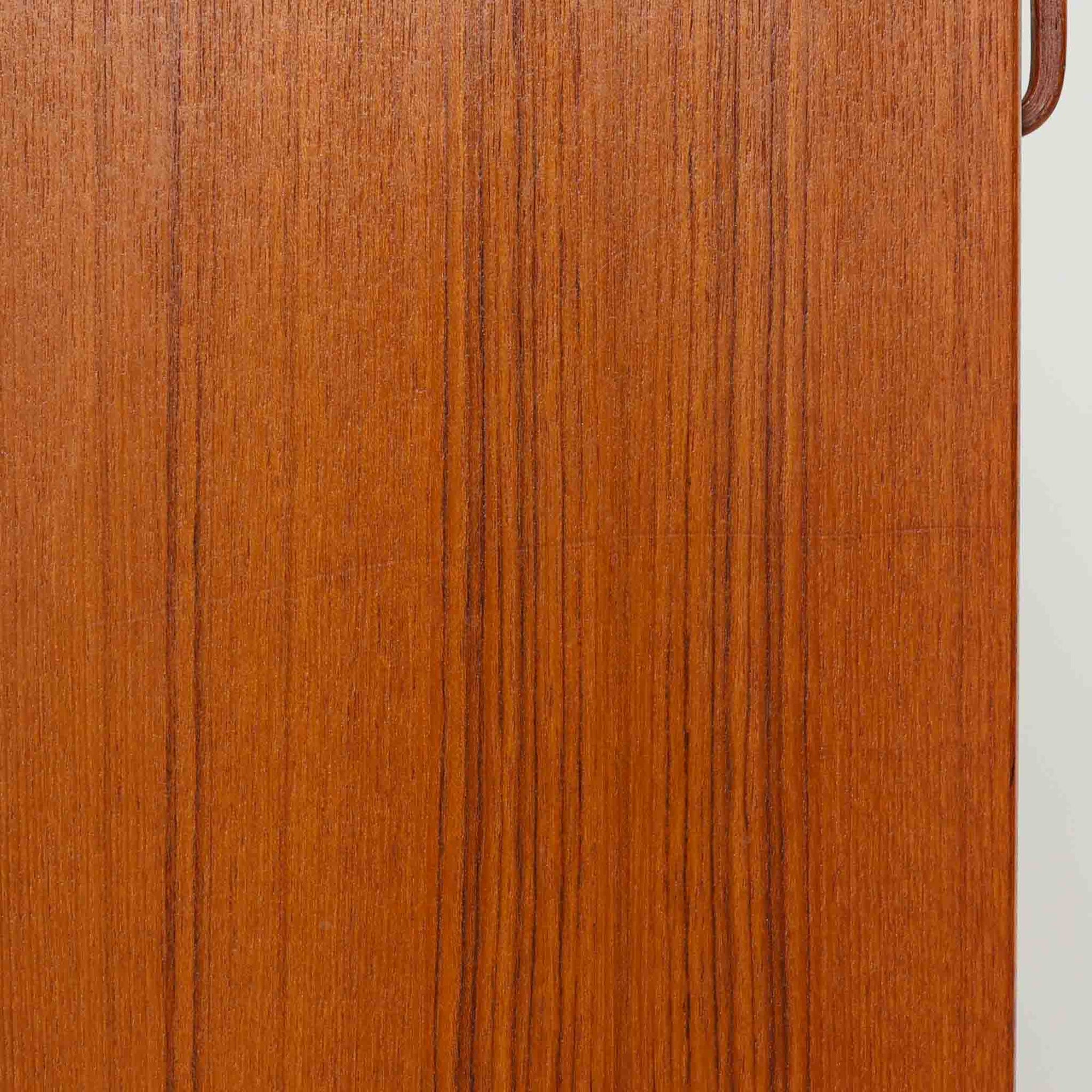 B.フリードホーゲンがデザインし、Bodafors社により製作された北欧ビンテージのディスプレイシェルフです。チーク材の美しい木目を活かした縦に伸びる端正なフレーム構成が印象的で、オープン棚と下部収納を組み合わせた実用性の高いデザインとなっています。上段は抜け感のある棚板構造で、書籍や器、オブジェを軽やかに飾ることができ、下段の引き戸収納は生活感の出やすい物をすっきりと収められます。脚付きによる軽快な佇まいと、経年変化によって深みを増した素材感が、空間に北欧ビンテージならではの落ち着いた存在感を与えます。