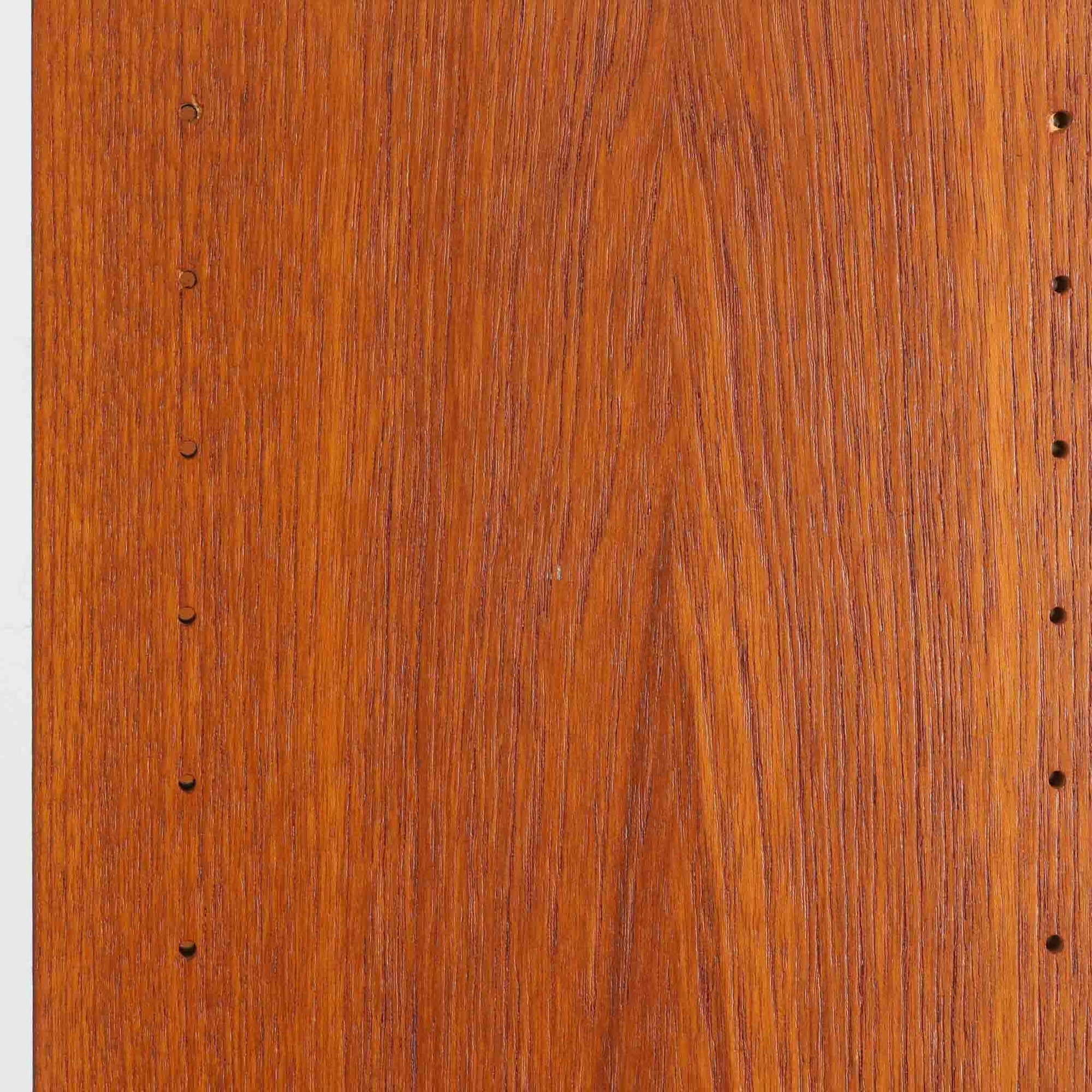 B.フリードホーゲンがデザインし、Bodafors社により製作された北欧ビンテージのディスプレイシェルフです。チーク材の美しい木目を活かした縦に伸びる端正なフレーム構成が印象的で、オープン棚と下部収納を組み合わせた実用性の高いデザインとなっています。上段は抜け感のある棚板構造で、書籍や器、オブジェを軽やかに飾ることができ、下段の引き戸収納は生活感の出やすい物をすっきりと収められます。脚付きによる軽快な佇まいと、経年変化によって深みを増した素材感が、空間に北欧ビンテージならではの落ち着いた存在感を与えます。