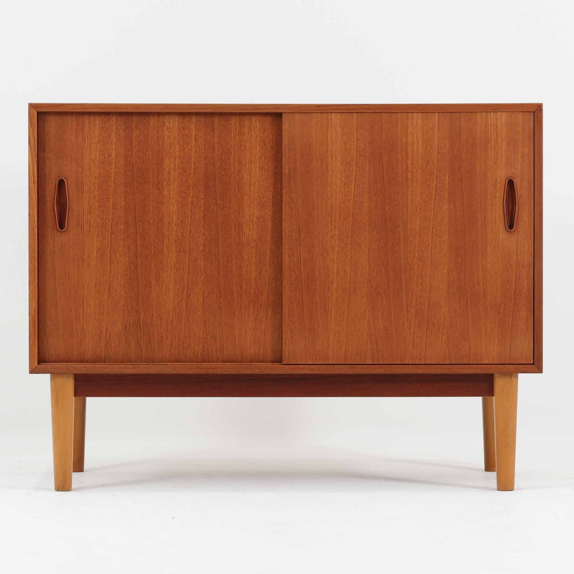 Nils Jonssonがデザインし、Hugo Troedsが製作した幅95cmの小ぶりなボードです。上質なチーク材を用いた端正な箱型フォルムに、楕円形の彫り込み取っ手がさりげないアクセントを添えています。引き戸仕様により限られた空間でも扱いやすく、内部には棚板を備え収納力も十分。すらりと伸びる脚部が軽やかな印象を与え、リビングや書斎、玄関先でも活躍します。経年により深みを増した木肌が北欧ビンテージならではの温もりと存在感を感じさせる一品です。