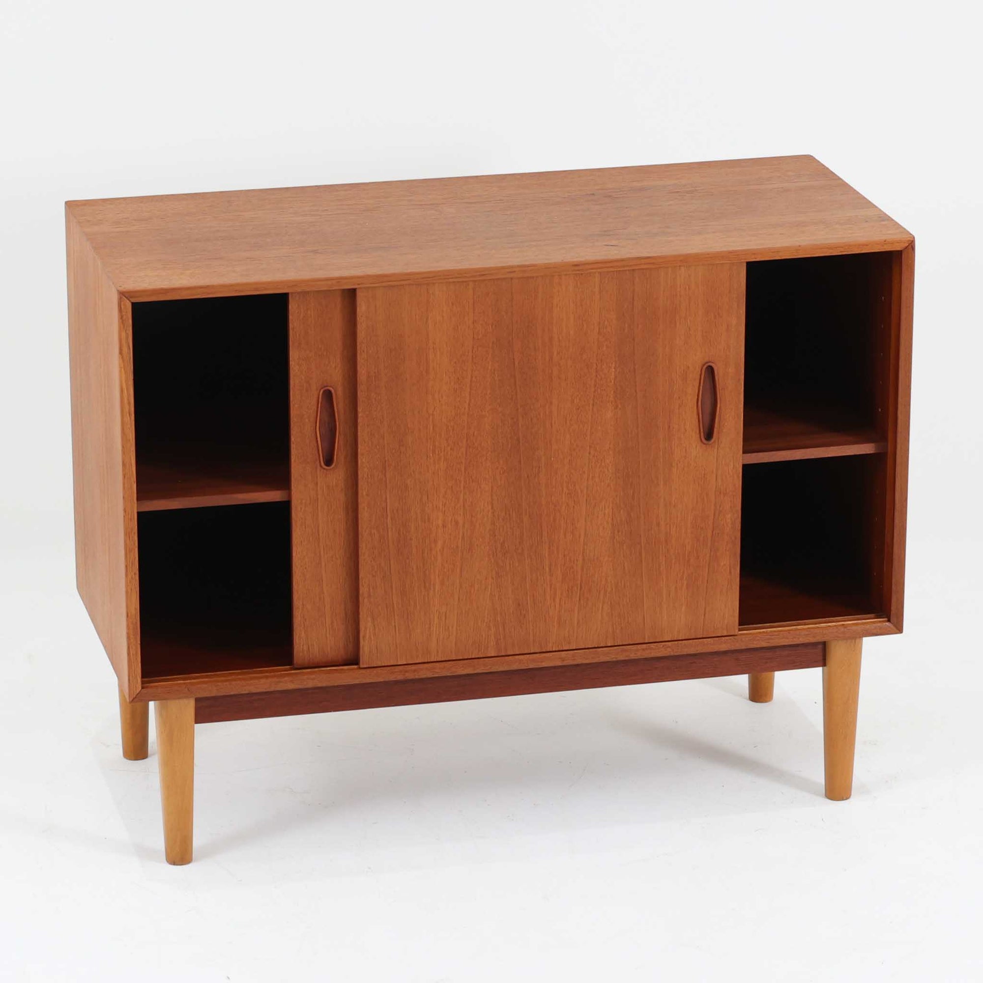 Nils Jonssonがデザインし、Hugo Troedsが製作した幅95cmの小ぶりなボードです。上質なチーク材を用いた端正な箱型フォルムに、楕円形の彫り込み取っ手がさりげないアクセントを添えています。引き戸仕様により限られた空間でも扱いやすく、内部には棚板を備え収納力も十分。すらりと伸びる脚部が軽やかな印象を与え、リビングや書斎、玄関先でも活躍します。経年により深みを増した木肌が北欧ビンテージならではの温もりと存在感を感じさせる一品です。