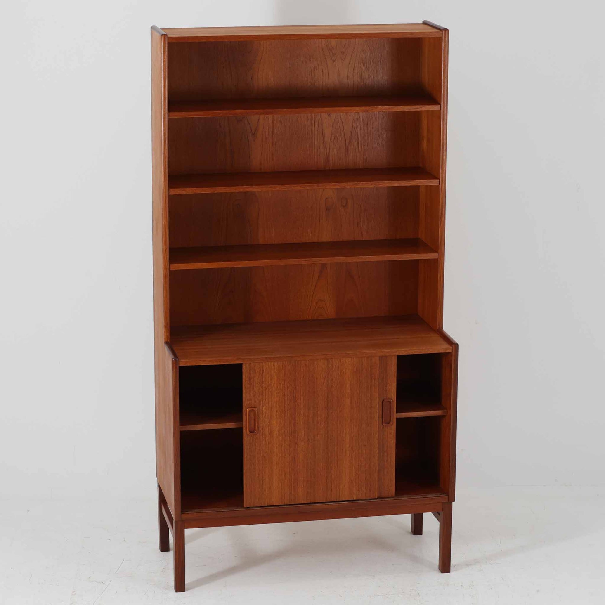 スウェーデン製のこちらのディスプレイシェルフは、チーク材の深みある木目が美しい上段のオープン棚と、下段のスライド扉収納を組み合わせた機能性の高い構成が特徴で、細身のフレームや角を丁寧に面取りした滑らかなフォルムが空間に柔らかな印象をもたらす北欧ビンテージ家具です。書籍や雑貨を見せながら収納でき、下段には日用品をすっきりと隠してしまえるため、リビングやダイニングの整理にも便利で、経年によって深まったチーク材の風合いがインテリアに温かみと落ち着きを添える一台です。