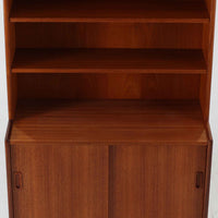 スウェーデン製のこちらのディスプレイシェルフは、チーク材の深みある木目が美しい上段のオープン棚と、下段のスライド扉収納を組み合わせた機能性の高い構成が特徴で、細身のフレームや角を丁寧に面取りした滑らかなフォルムが空間に柔らかな印象をもたらす北欧ビンテージ家具です。書籍や雑貨を見せながら収納でき、下段には日用品をすっきりと隠してしまえるため、リビングやダイニングの整理にも便利で、経年によって深まったチーク材の風合いがインテリアに温かみと落ち着きを添える一台です。