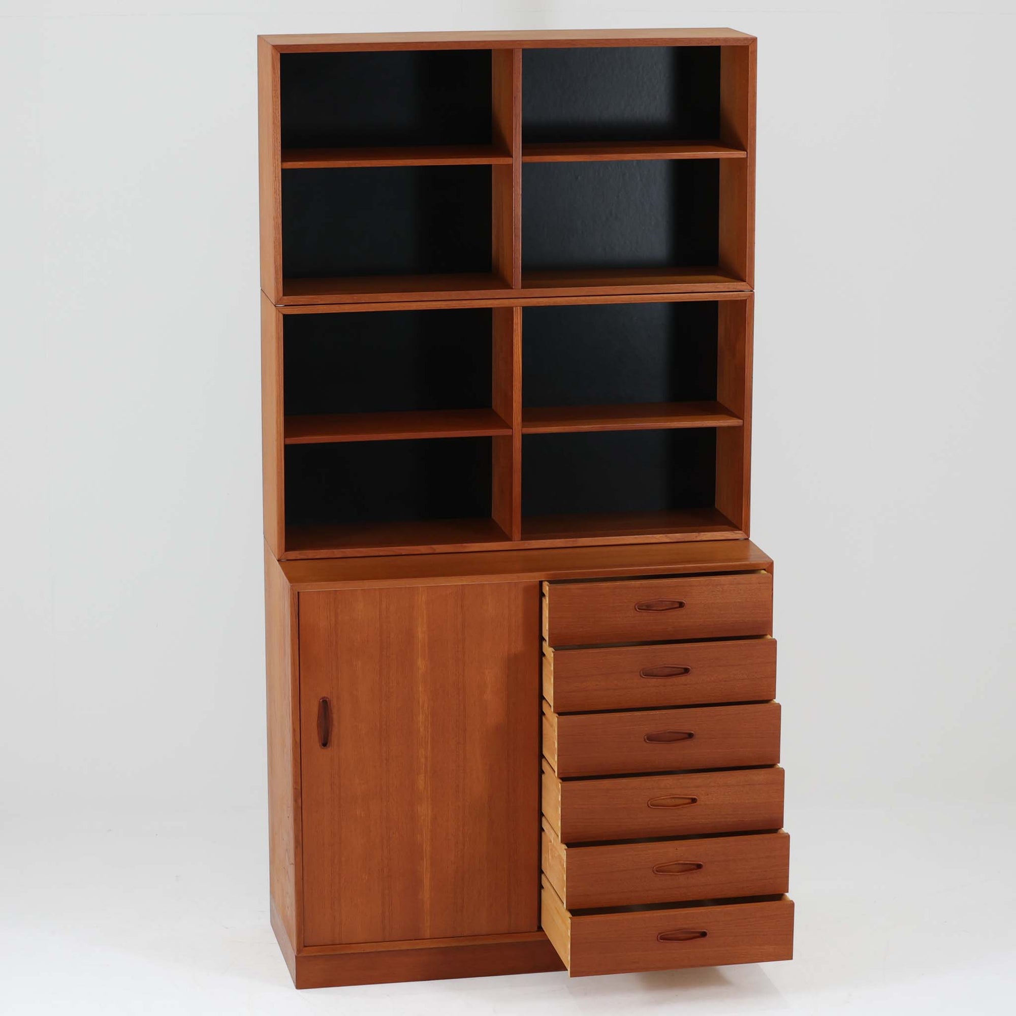 Nils Jonssonがデザインし、Hugo Troedsより発表されたモデルDomi 13のディスプレイシェルフです。チーク材の美しい木目と温かみのある色合いが空間に上質な北欧らしさをもたらします。上段・中段・下段のセクション構造で、それぞれを分けて使用できる柔軟な設計も魅力。下段は右側に引き出し、左側に高さ調整可能な棚を備え、実用性にも優れています。削り出しの取っ手や端正なフレームラインに職人技が感じられ、経年により深みを増した風合いがビンテージならではの存在感を放つ一品です。