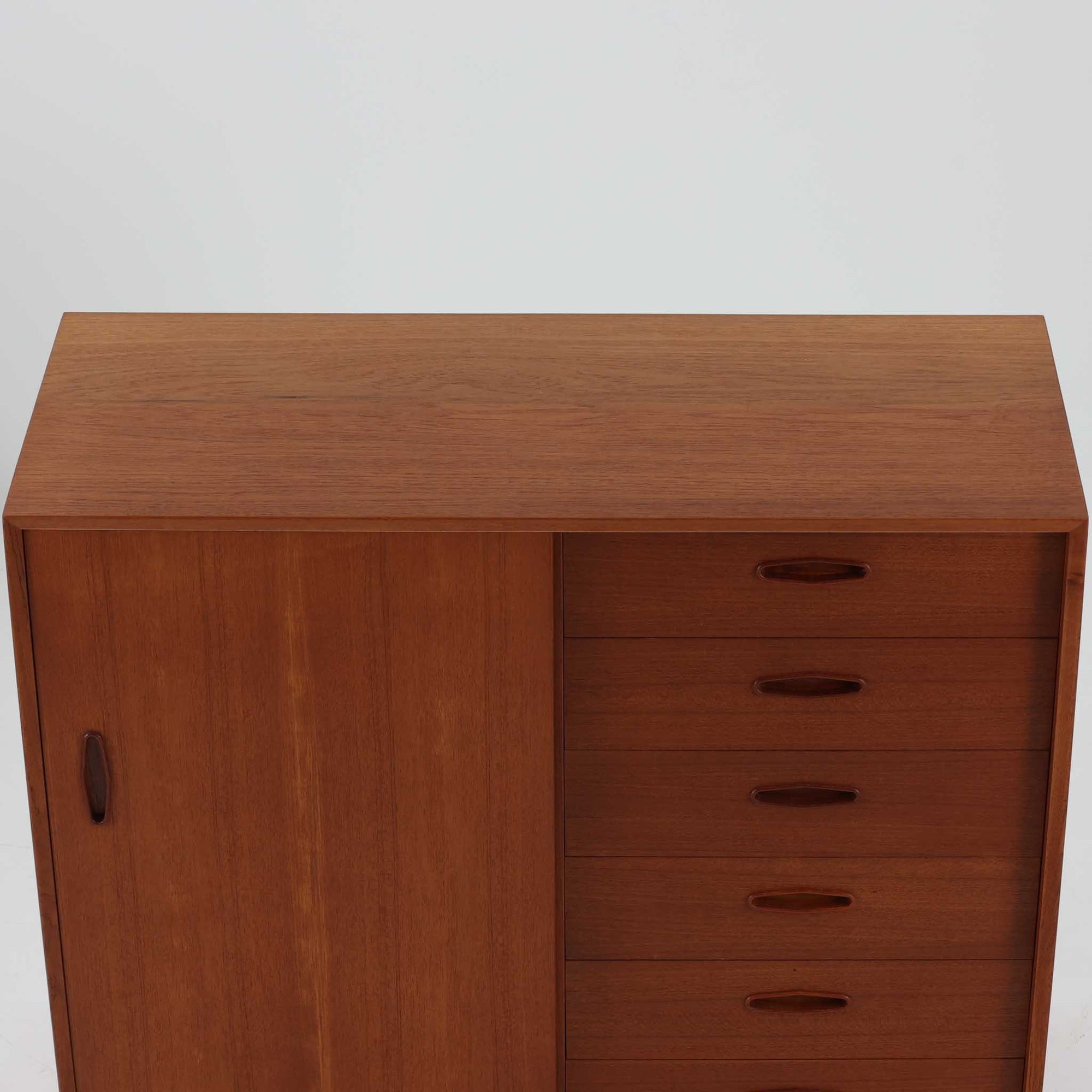 Nils Jonssonがデザインし、Hugo Troedsより発表されたモデルDomi 13のディスプレイシェルフです。チーク材の美しい木目と温かみのある色合いが空間に上質な北欧らしさをもたらします。上段・中段・下段のセクション構造で、それぞれを分けて使用できる柔軟な設計も魅力。下段は右側に引き出し、左側に高さ調整可能な棚を備え、実用性にも優れています。削り出しの取っ手や端正なフレームラインに職人技が感じられ、経年により深みを増した風合いがビンテージならではの存在感を放つ一品です。