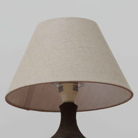 Chris HaslevがJetiのために手掛けたこちらのテーブルランプは、太陽を思わせるレリーフ模様をまとった陶器ベースと、素朴な土肌と釉薬の濃淡が織りなす豊かな表情が魅力で、コンパクトながら存在感を放つ北欧ビンテージ品です。上部のマットな質感が造形を引き締め、リネンシェード越しに広がるあたたかな灯りが空間をやさしく包み込み、リビングやベッドサイドのアクセントとして取り入れやすい一台に仕上がっています。