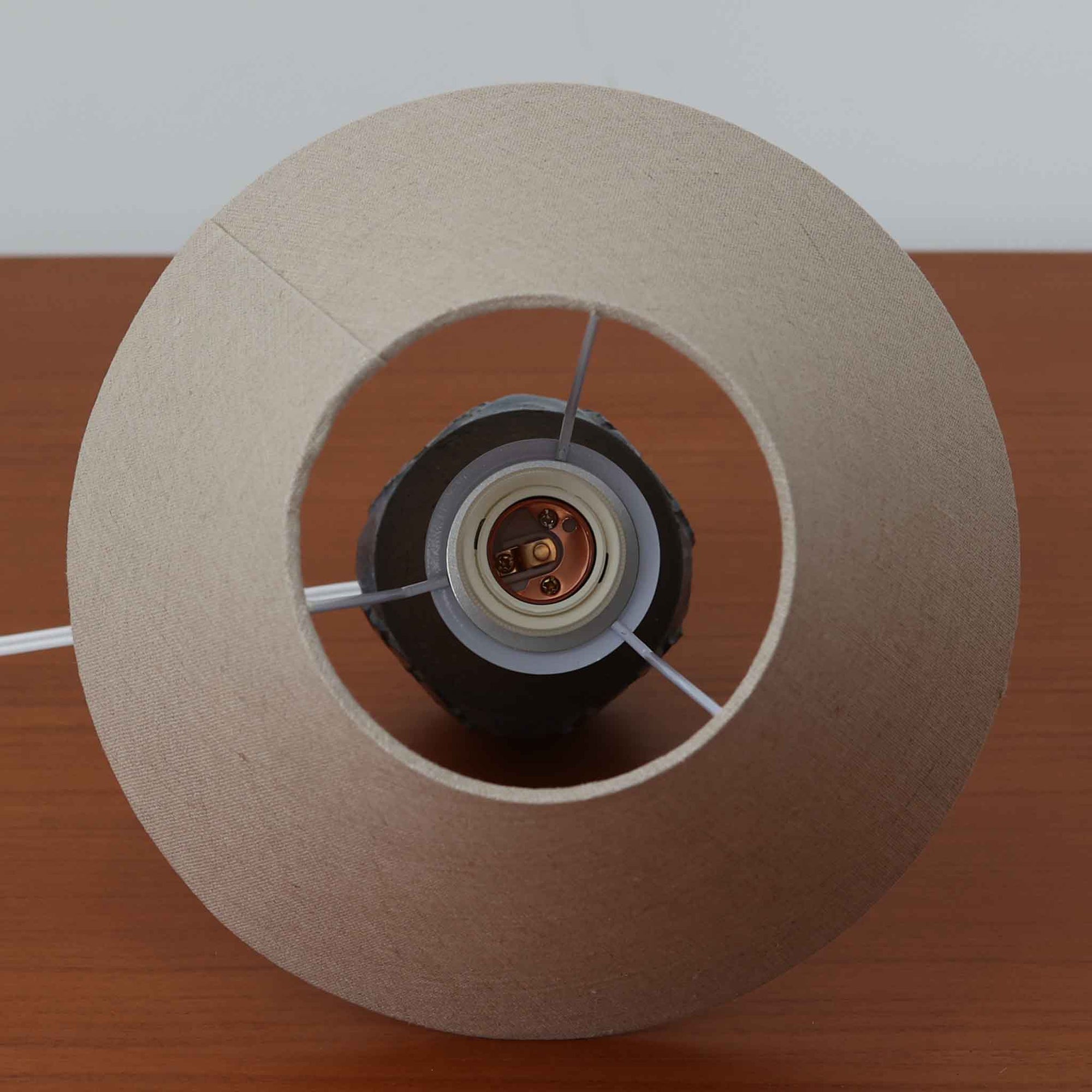 Chris HaslevがJetiのために手掛けたこちらのテーブルランプは、太陽を思わせるレリーフ模様をまとった陶器ベースと、素朴な土肌と釉薬の濃淡が織りなす豊かな表情が魅力で、コンパクトながら存在感を放つ北欧ビンテージ品です。上部のマットな質感が造形を引き締め、リネンシェード越しに広がるあたたかな灯りが空間をやさしく包み込み、リビングやベッドサイドのアクセントとして取り入れやすい一台に仕上がっています。