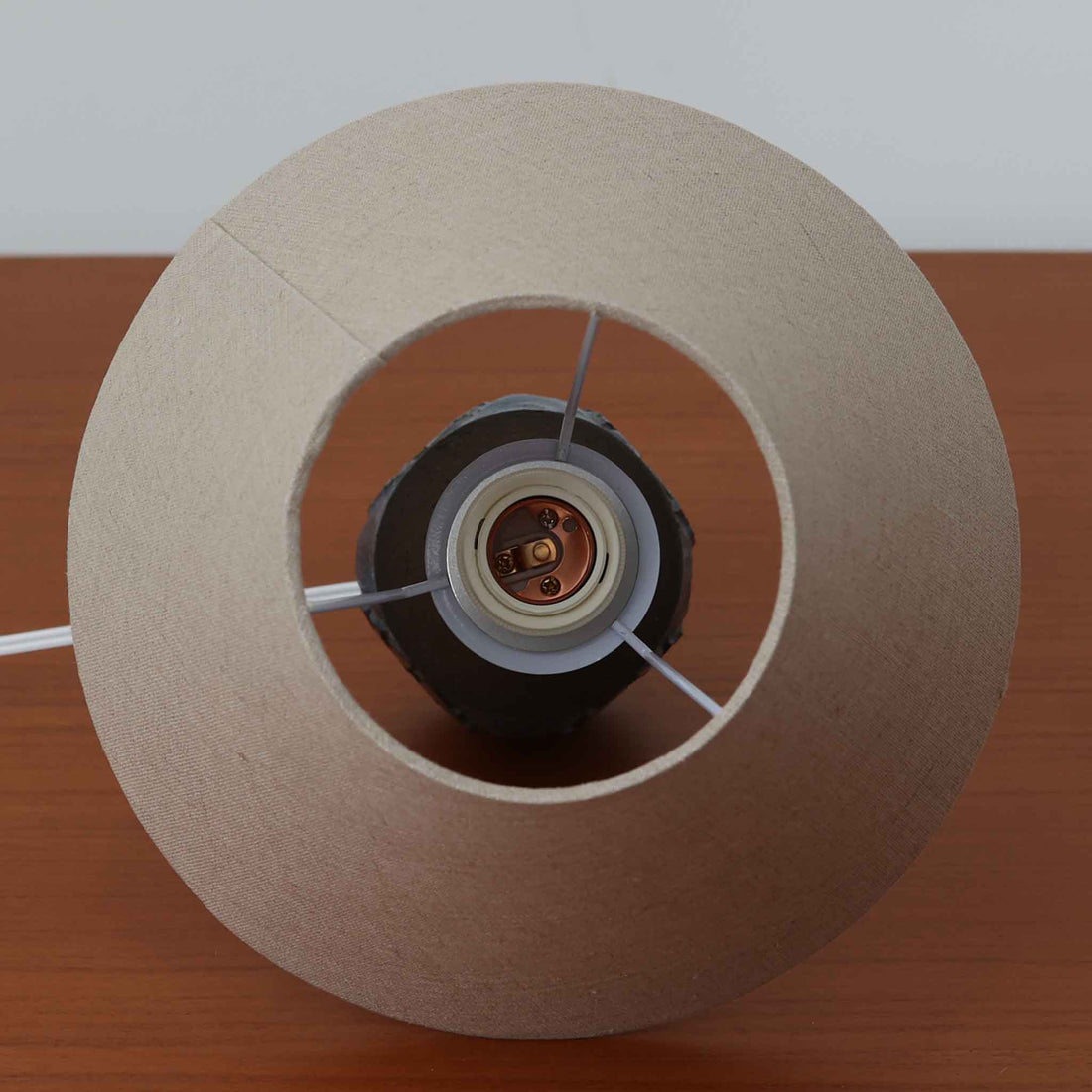 Chris HaslevがJetiのために手掛けたこちらのテーブルランプは、太陽を思わせるレリーフ模様をまとった陶器ベースと、素朴な土肌と釉薬の濃淡が織りなす豊かな表情が魅力で、コンパクトながら存在感を放つ北欧ビンテージ品です。上部のマットな質感が造形を引き締め、リネンシェード越しに広がるあたたかな灯りが空間をやさしく包み込み、リビングやベッドサイドのアクセントとして取り入れやすい一台に仕上がっています。