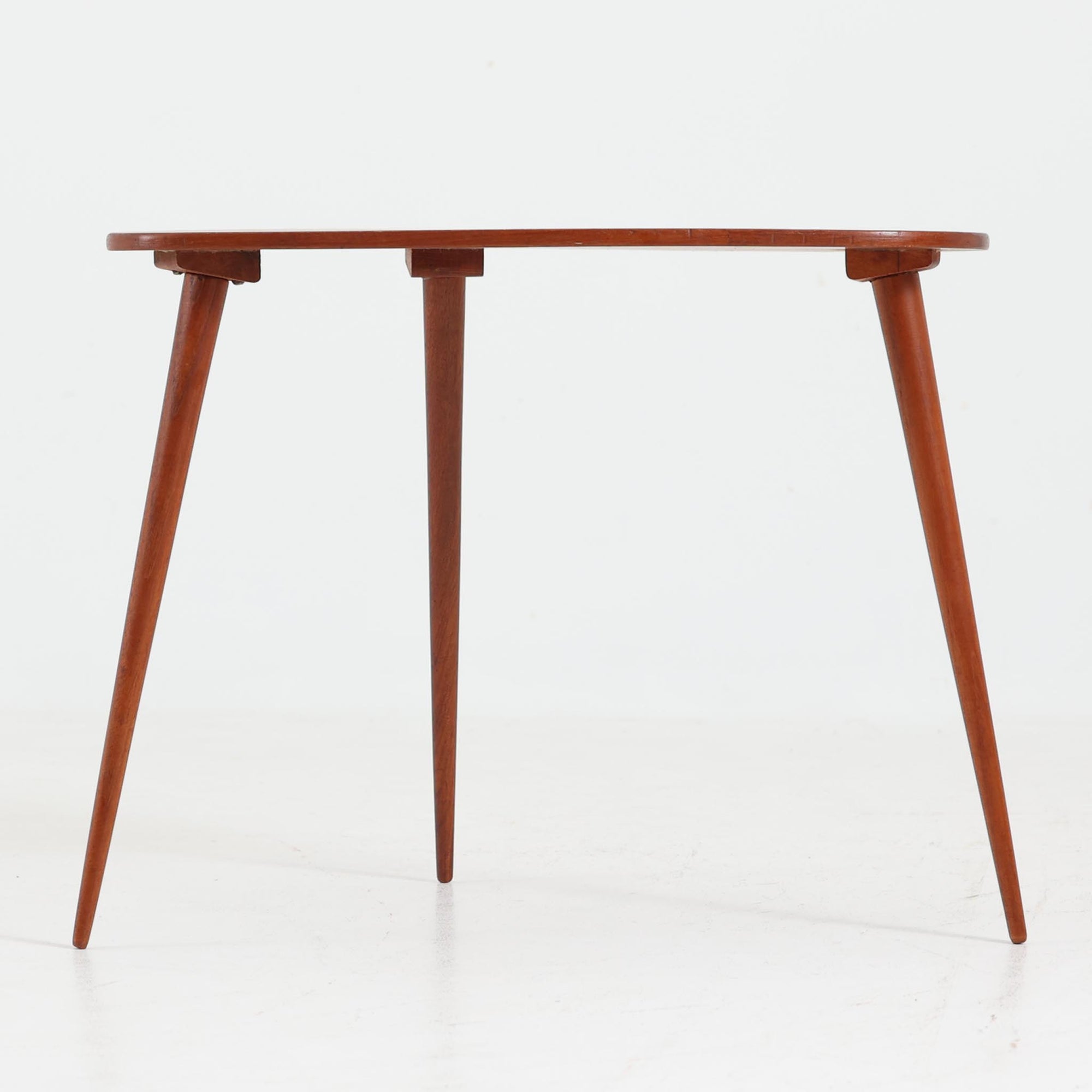 デンマーク製のチーク材サイドテーブルです。三角形に近い柔らかな曲線を描く天板と、すらりと伸びた3本脚が印象的なデザインで、ミッドセンチュリーらしい軽快な佇まいが魅力です。職人による丁寧な削り出しが際立ち、チーク材特有の深みある色合いと滑らかな手触りが楽しめます。コンパクトながら存在感があり、ソファ横やベッドサイドの小物置きとしても最適な一台です。