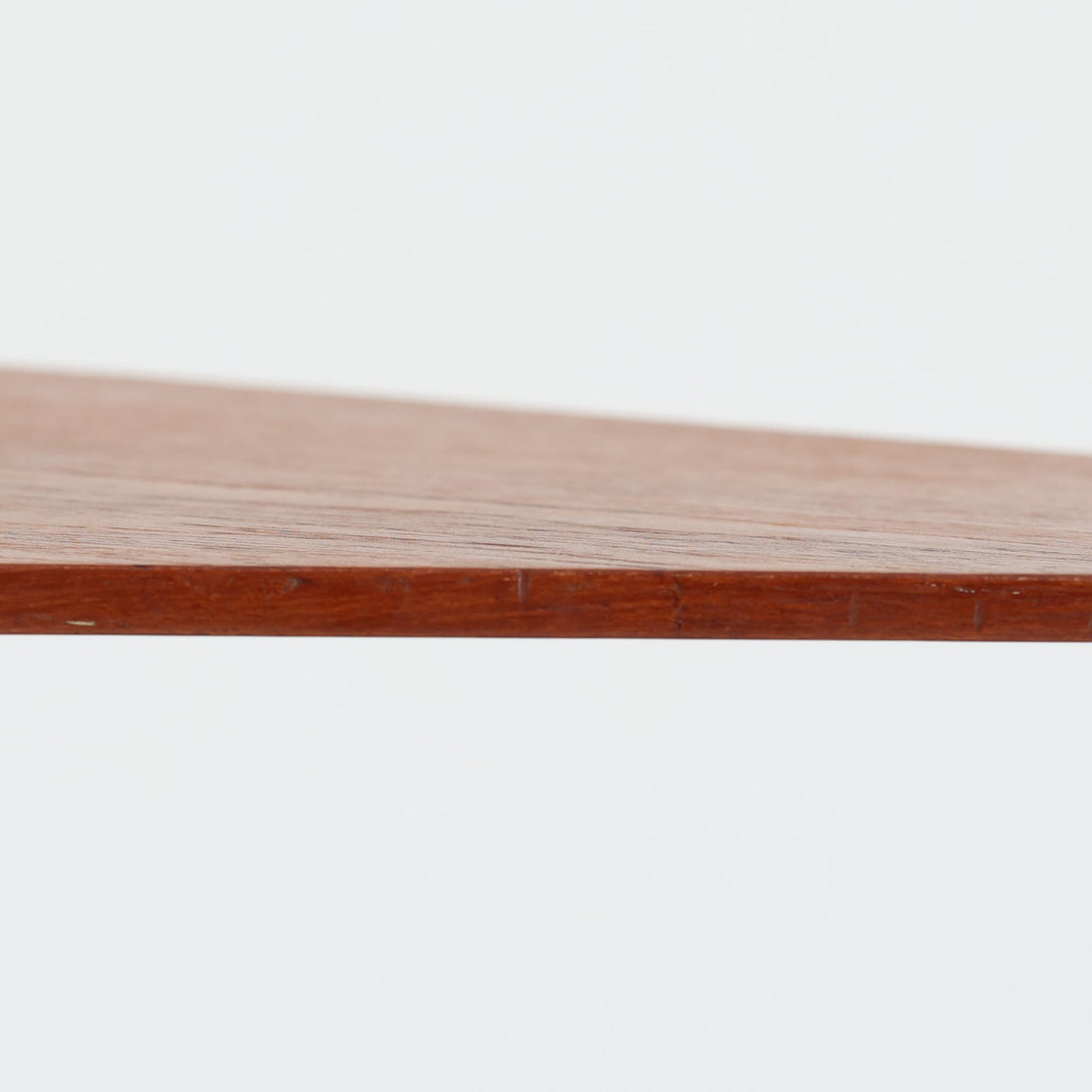 デンマーク製のチーク材サイドテーブルです。三角形に近い柔らかな曲線を描く天板と、すらりと伸びた3本脚が印象的なデザインで、ミッドセンチュリーらしい軽快な佇まいが魅力です。職人による丁寧な削り出しが際立ち、チーク材特有の深みある色合いと滑らかな手触りが楽しめます。コンパクトながら存在感があり、ソファ横やベッドサイドの小物置きとしても最適な一台です。