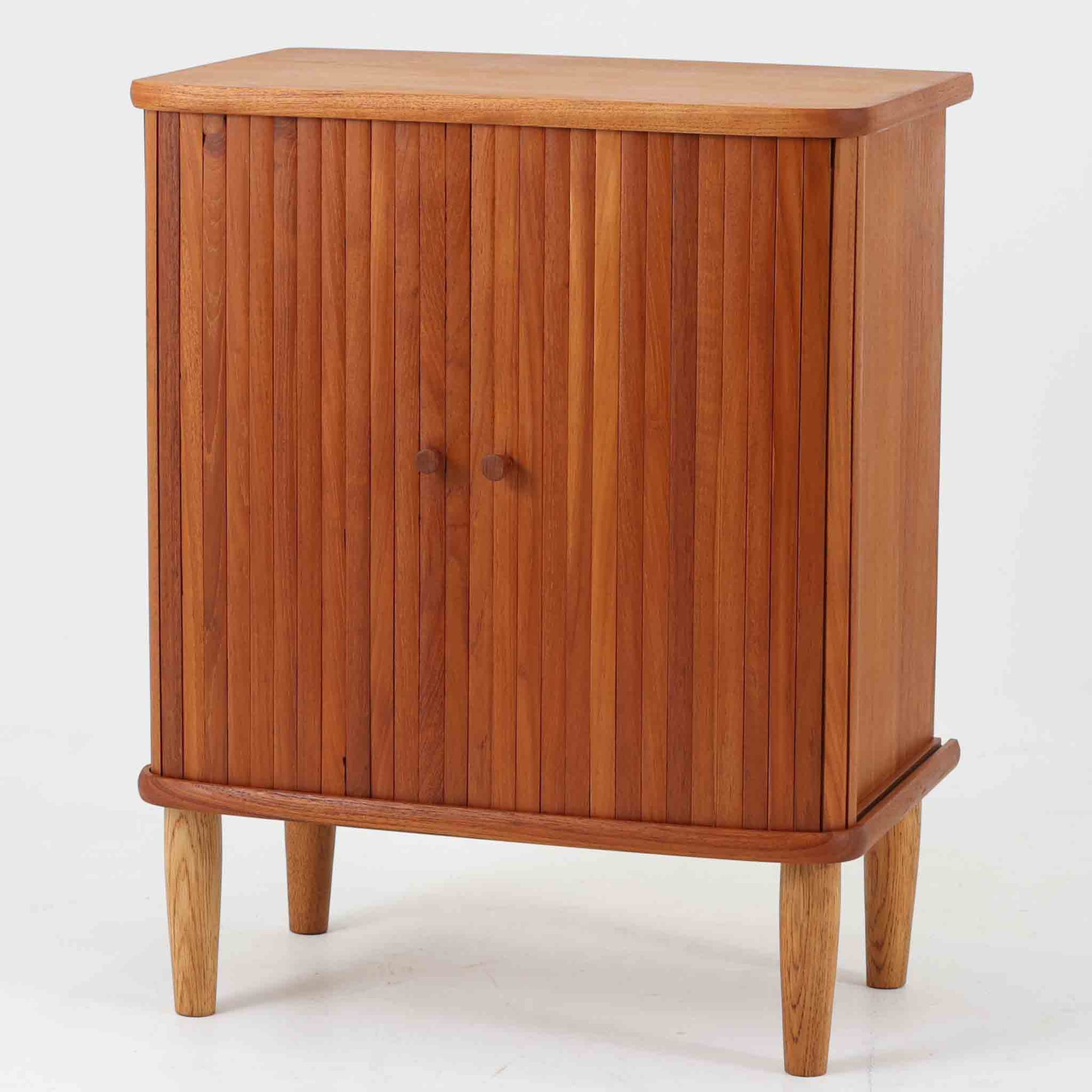 デンマーク製蛇腹キャビネット。チーク材の深みある木肌を活かした美しい縦桟の蛇腹扉が印象的で、開閉の所作そのものに北欧ビンテージらしい職人技を感じられる一台です。丸みを持たせた天板と台輪、軽やかな脚部のバランスが美しく、幅54cmのコンパクトなサイズ感でリビングや書斎、ベッドサイドにも取り入れやすい設計。内部は棚板付きで書類や日用品、小物をすっきり収納でき、見せたくない生活感を美しく隠しながら空間に上質な温もりを添えてくれます。