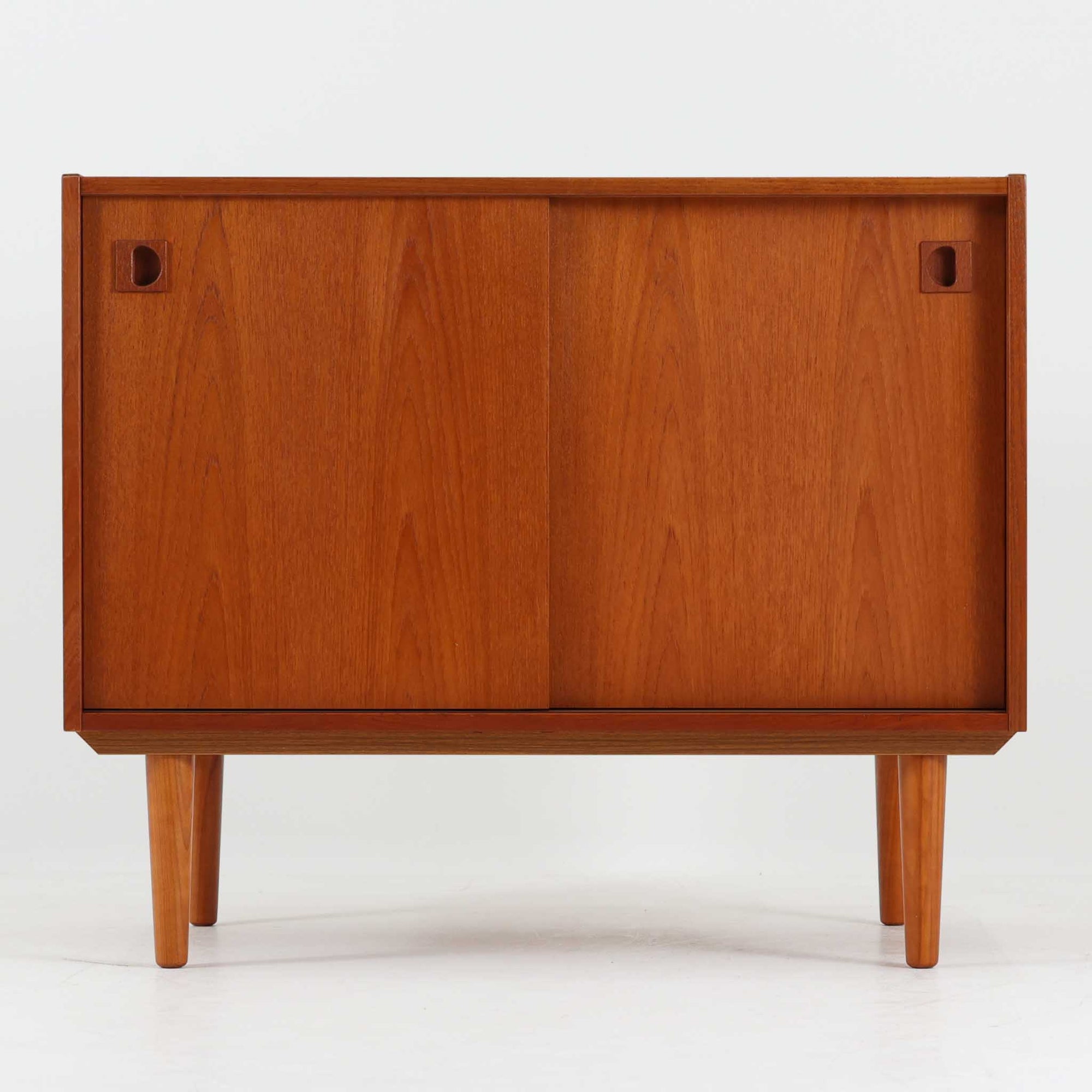 デンマーク製ボードです。チーク材の美しい木目と経年による深みのある色艶が魅力で、すっきりとした直線的なフォルムに北欧らしい洗練された佇まいが感じられます。前面には引き戸を備え、左右にスライドすることで内部の収納物へスムーズにアクセス可能。内部には棚板を設け、食器や雑貨、書類などを整理しやすい実用的な構造です。丸みを帯びた取手や細身の脚部が軽やかな印象を添え、リビングやダイニングで上質な収納家具として活躍する一台です。