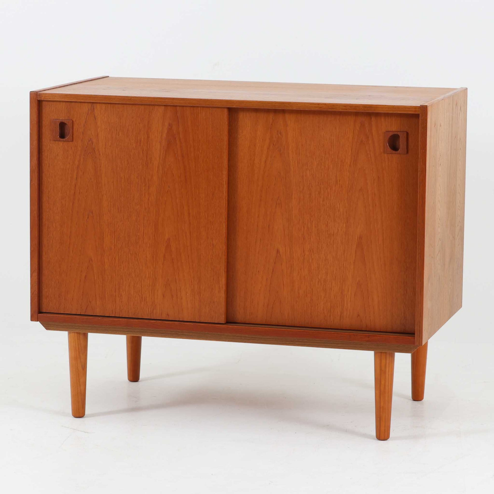 デンマーク製ボードです。チーク材の美しい木目と経年による深みのある色艶が魅力で、すっきりとした直線的なフォルムに北欧らしい洗練された佇まいが感じられます。前面には引き戸を備え、左右にスライドすることで内部の収納物へスムーズにアクセス可能。内部には棚板を設け、食器や雑貨、書類などを整理しやすい実用的な構造です。丸みを帯びた取手や細身の脚部が軽やかな印象を添え、リビングやダイニングで上質な収納家具として活躍する一台です。