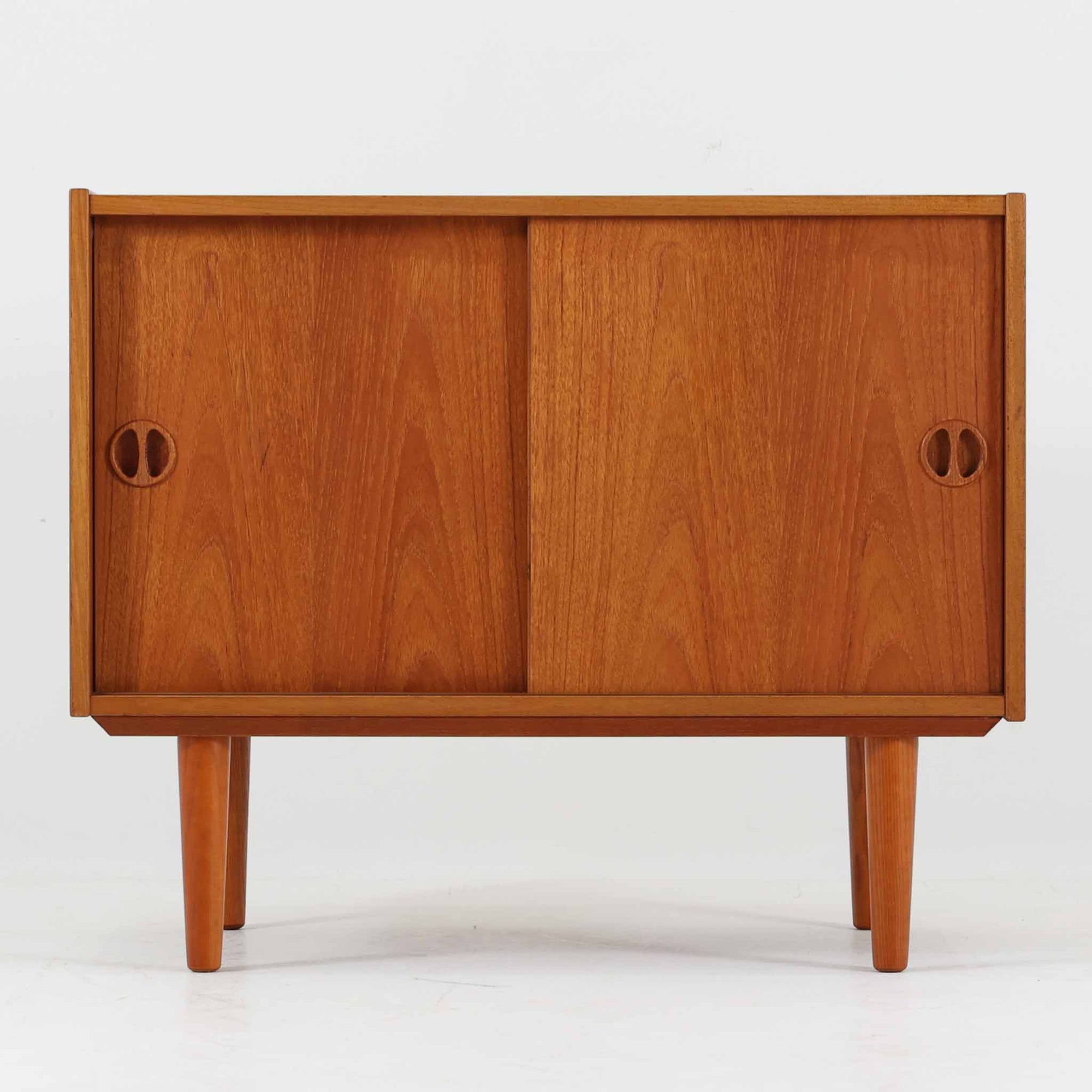 デンマーク製ボードです。チーク材の美しい木目と経年によって深みを増した色艶が魅力で、シンプルな箱型フォルムに丸みを帯びた取手がさりげないアクセントとなっています。引き戸仕様により限られたスペースでも使いやすく、内部には棚板を備え収納力と実用性を兼備。すっきりとした脚部が軽やかな印象を与え、リビングやダイニングで上質な収納家具として活躍する一台です。ビンテージならではの風合いと丁寧な作りが感じられます。