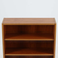 デンマーク製ブックシェルフです。小ぶりなサイズ感で扱いやすく、チーク材ならではの深みある木目と、縁にあしらわれた明るい木部のコントラストが北欧らしい端正な表情を生み出しています。無駄を削ぎ落としたシンプルな構造は圧迫感が少なく、書籍はもちろん、お気に入りの雑貨やオブジェを飾るディスプレイ棚としても活躍。リビングや寝室、デスク横にも取り入れやすく、経年で増した木肌の風合いが空間に穏やかな温もりとビンテージならではの存在感を添える一台です。