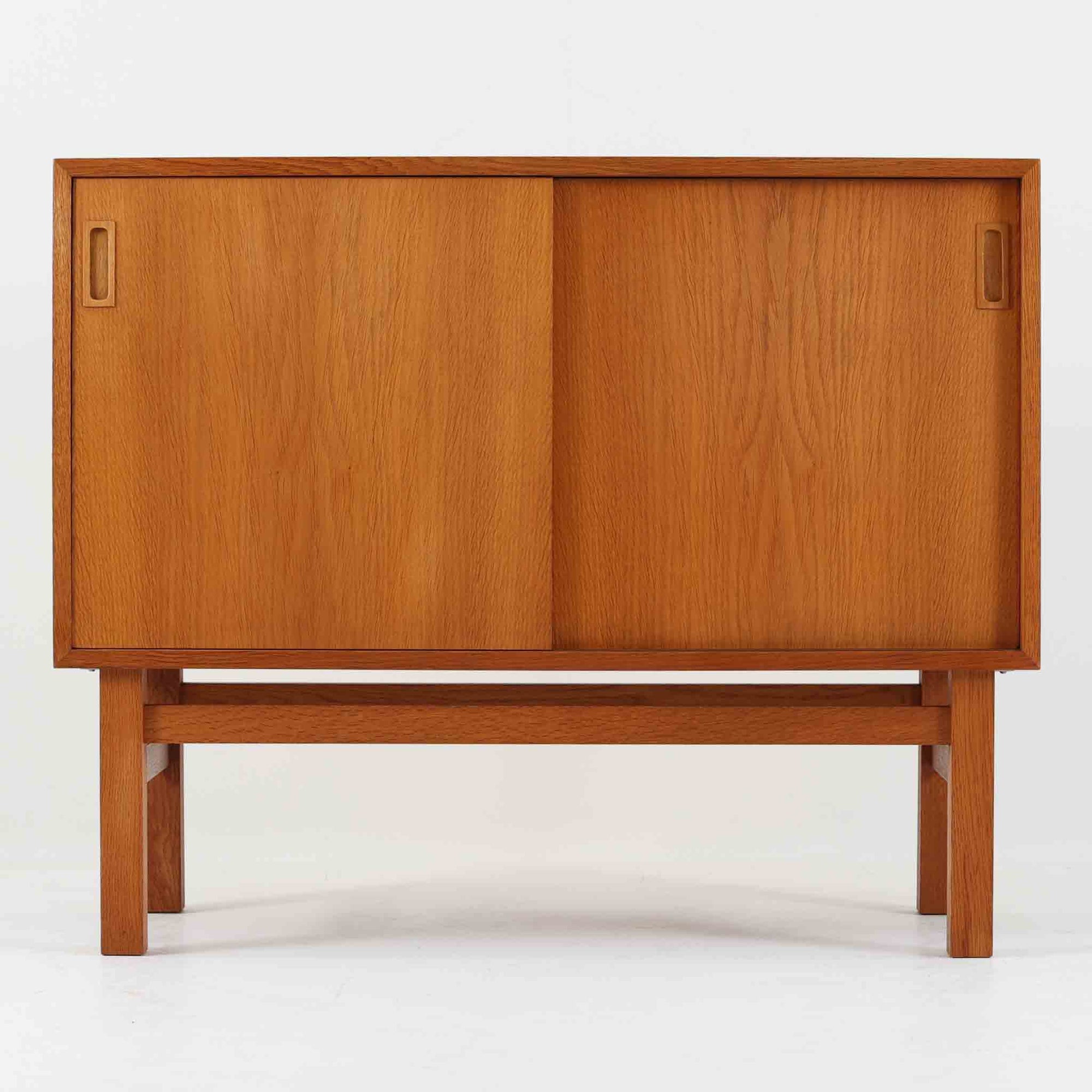 Vitre（ヴィトレ）によるデンマーク製のオーク材ボードです。幅90cmの取り入れやすいサイズ感に、すっきりとした引き戸と細身の脚部を組み合わせた端正な佇まいが北欧らしい一台。内部にはスライド式のトレイが備えられており、書類や小物を整理しやすく、リビングの収納家具としてはもちろん、デスク脇でのキャビネットやショップ什器としても活躍します。経年により深みを増したオークの木肌と丁寧な造りが、ビンテージならではの上質な存在感を演出し、実用性と意匠性を兼ね備えた希少性のある収納家具です。