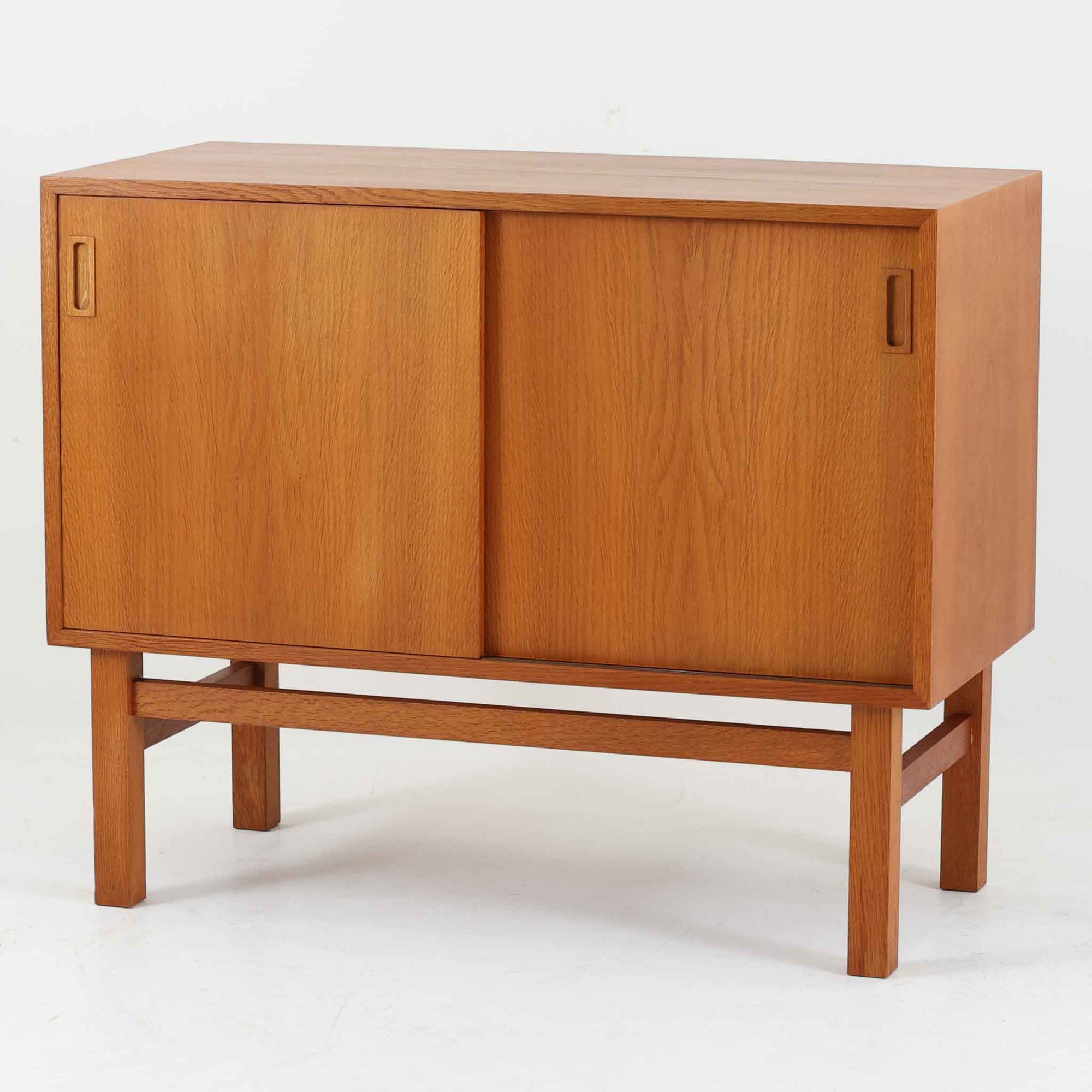 Vitre（ヴィトレ）によるデンマーク製のオーク材ボードです。幅90cmの取り入れやすいサイズ感に、すっきりとした引き戸と細身の脚部を組み合わせた端正な佇まいが北欧らしい一台。内部にはスライド式のトレイが備えられており、書類や小物を整理しやすく、リビングの収納家具としてはもちろん、デスク脇でのキャビネットやショップ什器としても活躍します。経年により深みを増したオークの木肌と丁寧な造りが、ビンテージならではの上質な存在感を演出し、実用性と意匠性を兼ね備えた希少性のある収納家具です。