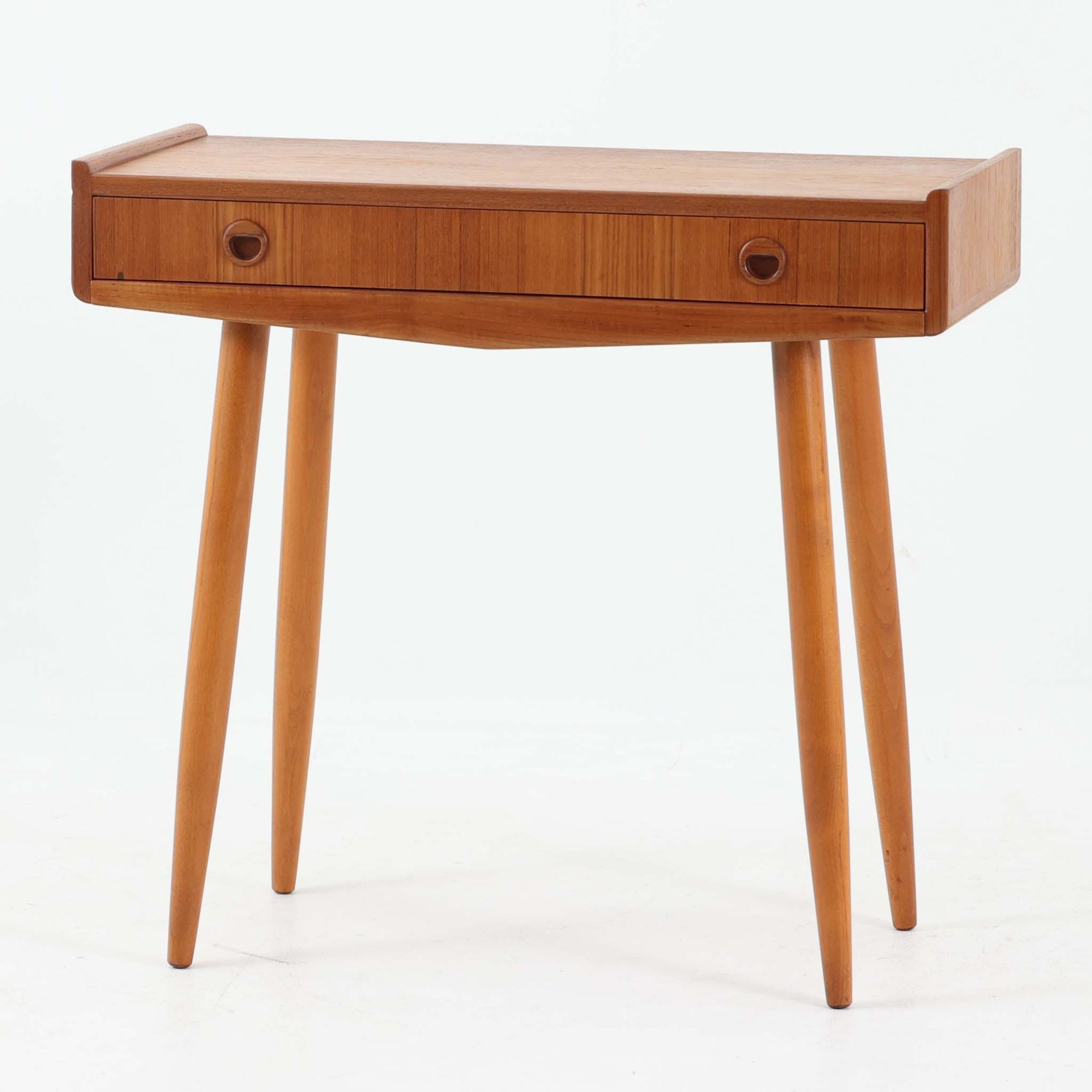 スウェーデン製のサイドチェストです。チーク材とビーチ材を組み合わせた温かみのある素材使いが特徴で、天板の立ち上がりや丸みを帯びた縁取りがやわらかな印象を与えます。前面には引き出しが備えられ、小物の整理に便利な実用性も魅力。すっきりと伸びたテーパー脚が軽やかさを添え、リビングやベッドサイド、玄関先など幅広いシーンで活躍します。経年により深みを増した木肌と丁寧な造りが、北欧ビンテージならではの落ち着いた存在感を演出する一台です。