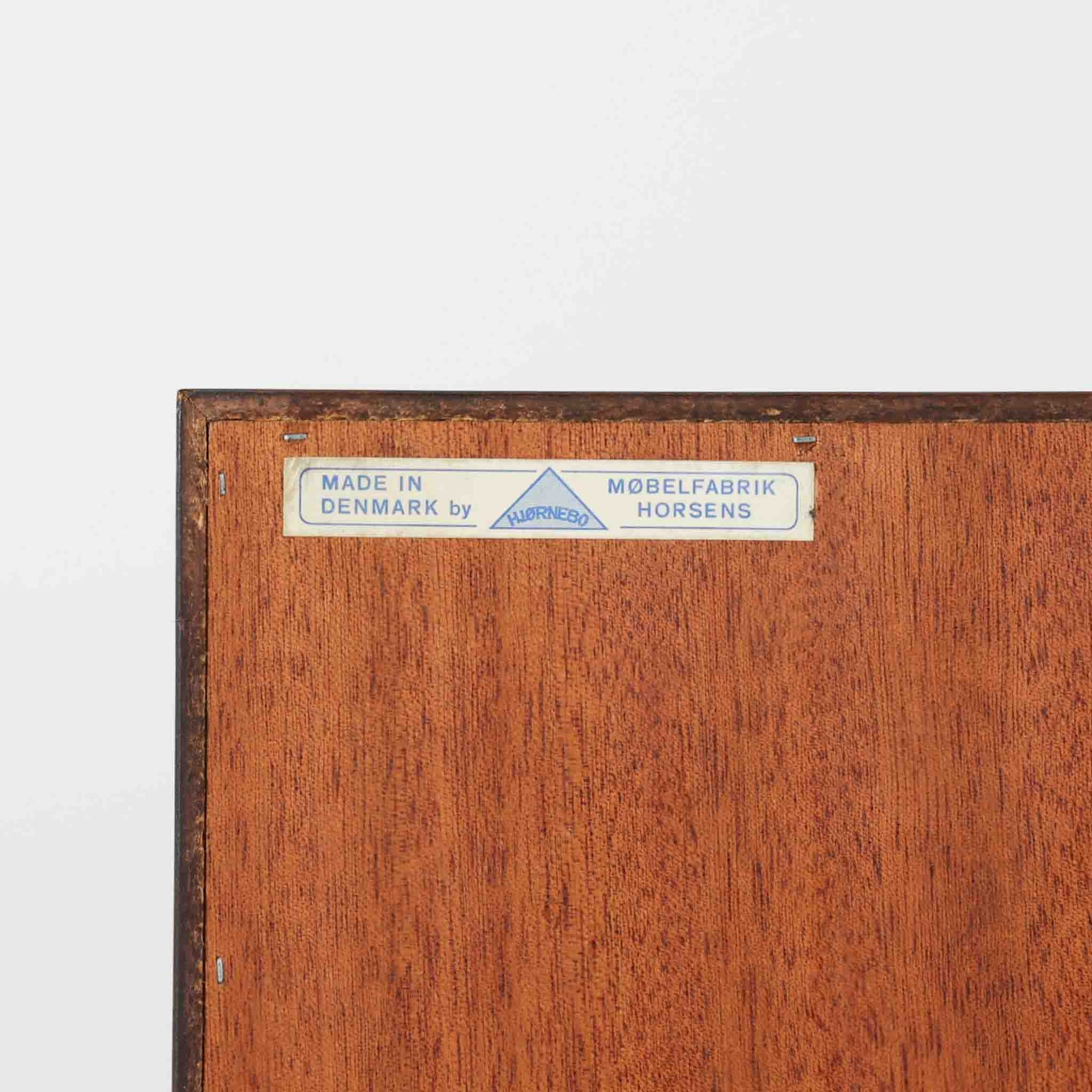 Hjornebo Mobelfabrik（ヒョルネボ・モーベルファブリック）によるデンマーク製のチーク材ブックシェルフです。幅86cmの使いやすいサイズに、すっきりとしたオープン構造と丸みを帯びた脚部を組み合わせた、軽やかな北欧デザインが魅力の一台。内部は2枚の棚板で実用的に仕切られ、書籍や雑誌の収納はもちろん、オブジェや器、オーディオ機器を飾るディスプレイシェルフとしても美しく映えます。背板には配線穴が設けられており、AVボードやサイドボード感覚でも取り入れやすい設計。経年により深みを増したチークの美しい木目と丁寧な造りが、ビンテージならではの上質な存在感と希少性を空間にもたらします。