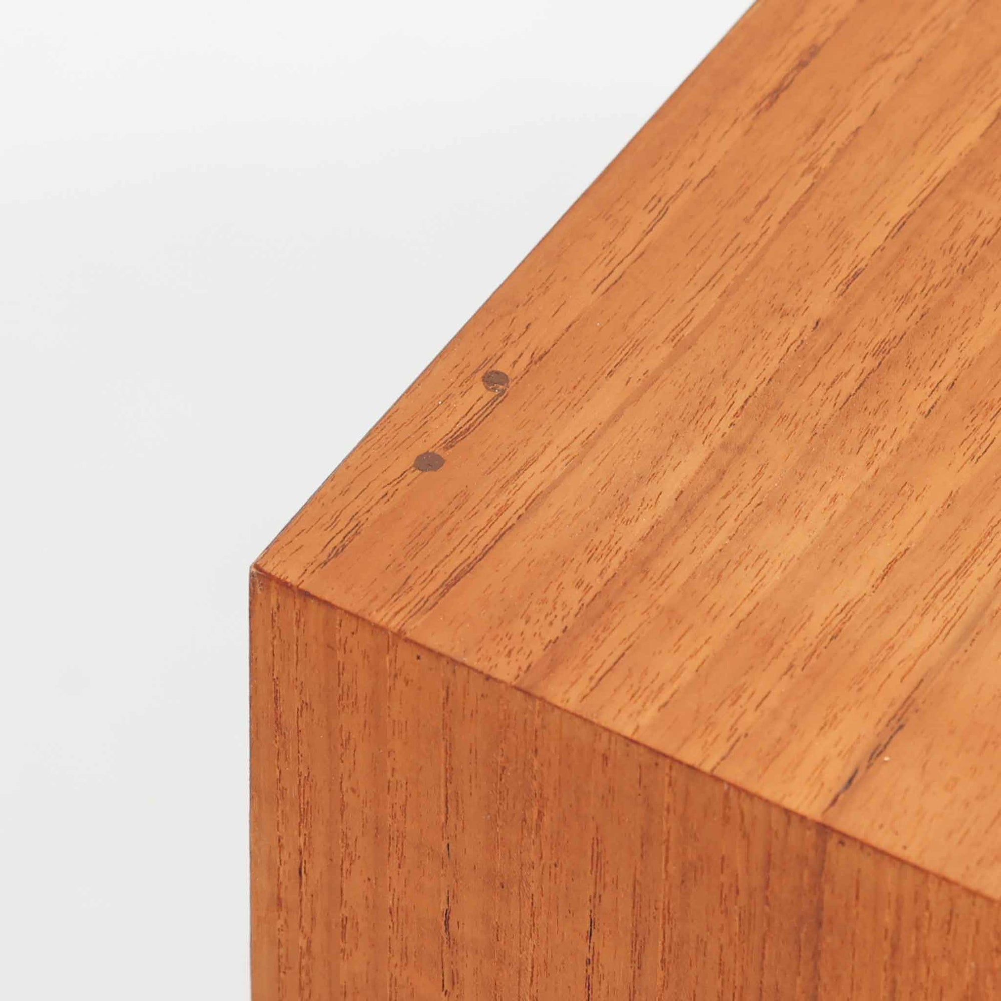 デンマークで製作されたチーク材のローボードです。幅100cmの小ぶりなサイズながら、温かみのある木目とシンプルな直線的フォルムが北欧らしい落ち着いた佇まいを演出します。前面には手掛け付きのスライド扉が備えられ、内部収納をすっきりと隠しながら使いやすさも確保。細身の脚部が軽やかな印象を与え、リビングや玄関、ベッドサイドなど様々な空間で活躍します。背板には壁掛け用の金具が取り付けられており、収納内部にはDIYによる木材の追加や小さな穴が見られますが、ビンテージ品ならではの味わいとして楽しめる一台です。