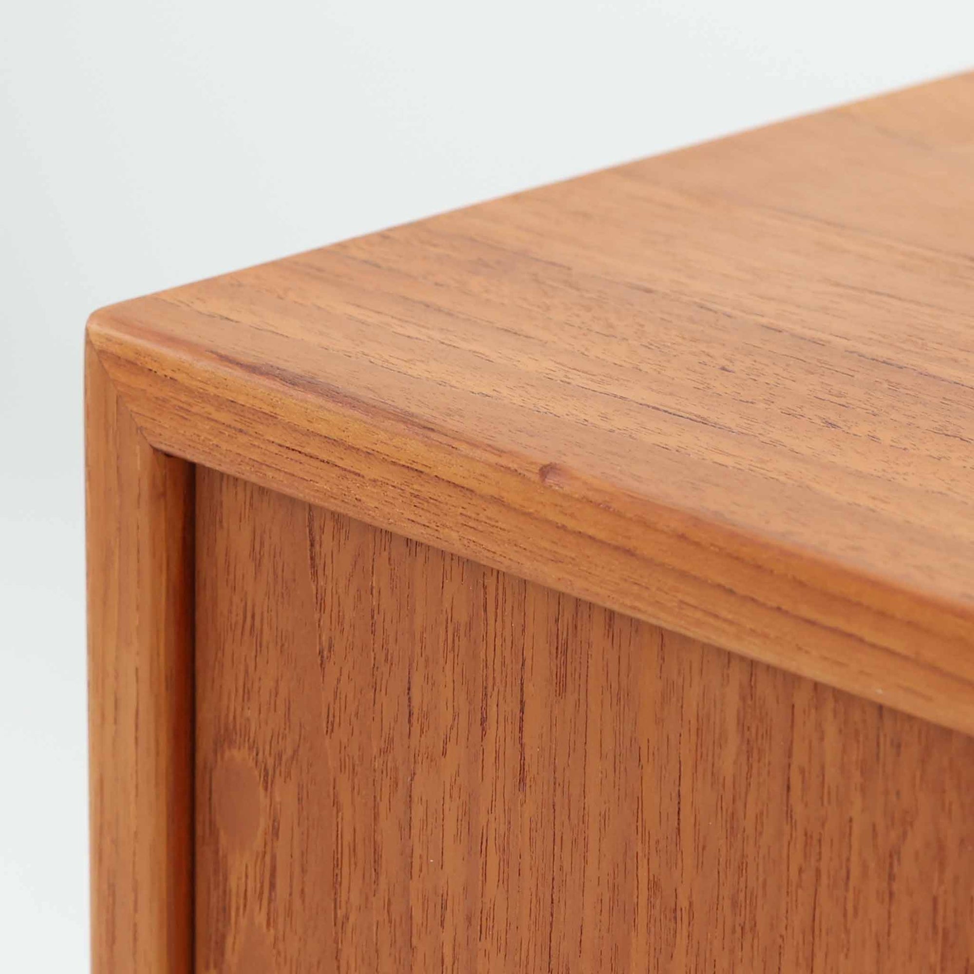 デンマークで製作されたチーク材のローボードです。幅100cmの小ぶりなサイズながら、温かみのある木目とシンプルな直線的フォルムが北欧らしい落ち着いた佇まいを演出します。前面には手掛け付きのスライド扉が備えられ、内部収納をすっきりと隠しながら使いやすさも確保。細身の脚部が軽やかな印象を与え、リビングや玄関、ベッドサイドなど様々な空間で活躍します。背板には壁掛け用の金具が取り付けられており、収納内部にはDIYによる木材の追加や小さな穴が見られますが、ビンテージ品ならではの味わいとして楽しめる一台です。
