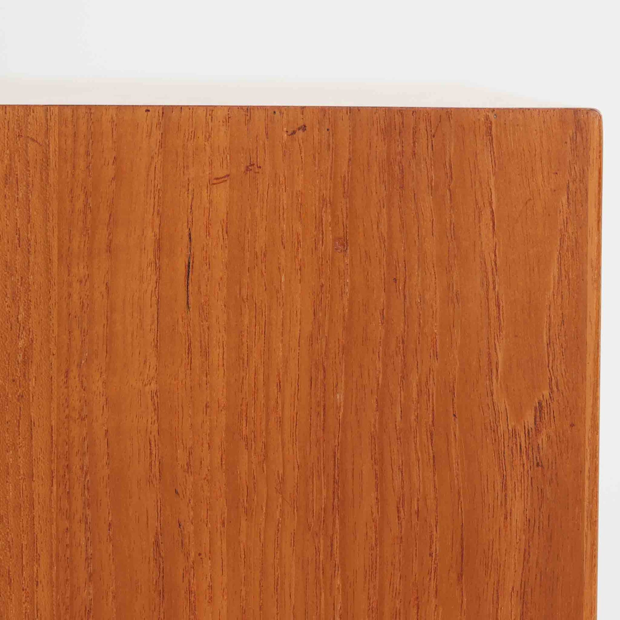 デンマークで製作されたチーク材のローボードです。幅100cmの小ぶりなサイズながら、温かみのある木目とシンプルな直線的フォルムが北欧らしい落ち着いた佇まいを演出します。前面には手掛け付きのスライド扉が備えられ、内部収納をすっきりと隠しながら使いやすさも確保。細身の脚部が軽やかな印象を与え、リビングや玄関、ベッドサイドなど様々な空間で活躍します。背板には壁掛け用の金具が取り付けられており、収納内部にはDIYによる木材の追加や小さな穴が見られますが、ビンテージ品ならではの味わいとして楽しめる一台です。